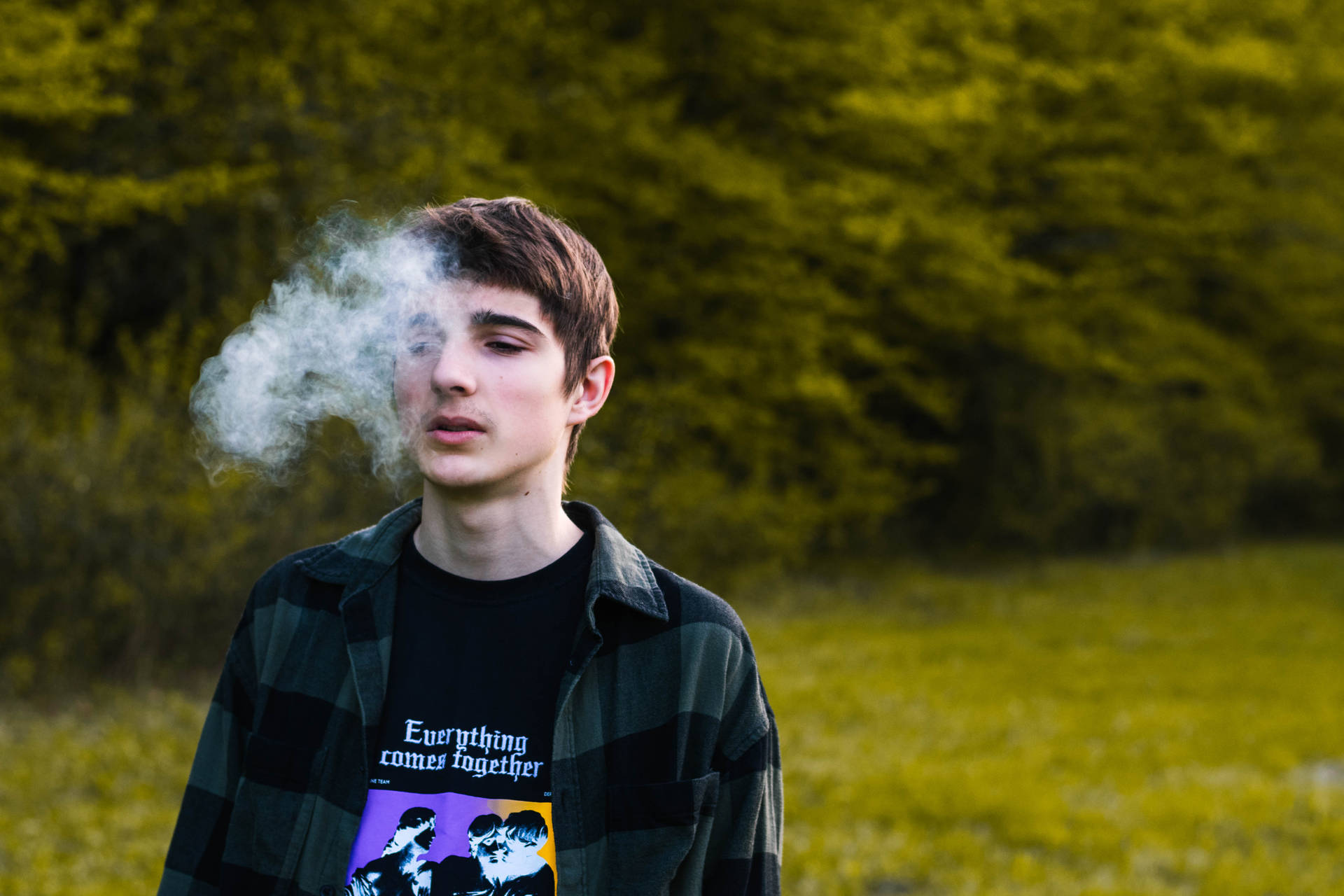 年輕男子在綠色森林中呼出煙霧。