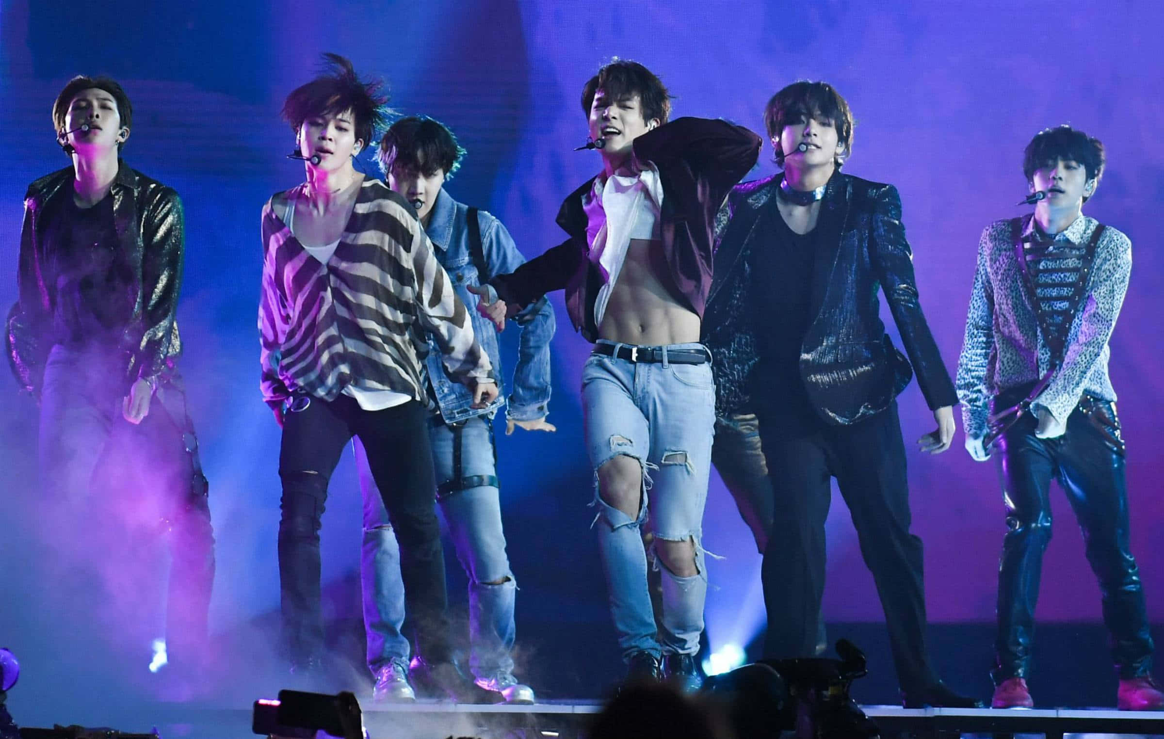 Bts Performance 桌布 壁紙 — 六位男表演者穿著時尚破洞牛仔褲和閃亮外套，在充滿活力的紫色和藍色舞台燈光及煙霧效果下充滿活力地跳舞。
