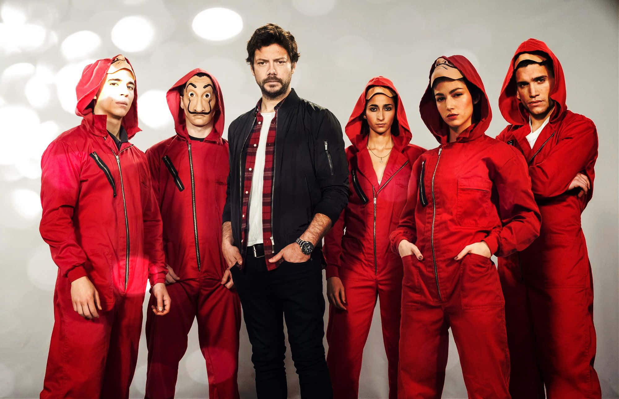 Money Heist 桌布 壁紙 — 六個身穿標誌性紅色連身衣和面具的人物站在一個身後有柔和發光燈光的攝影棚中。