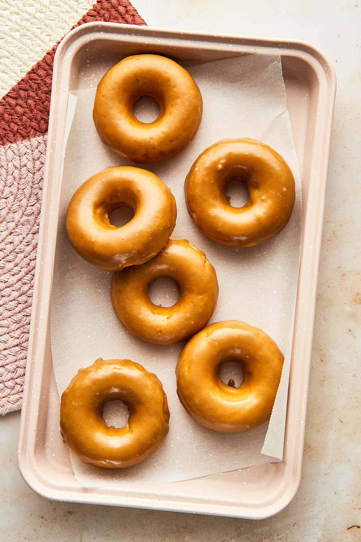 Glazed Donut 桌布 壁紙 — 六個釉面冬甩放在粉紅色托盤的牛油紙上，旁邊有一塊有紋理的粉白色布。