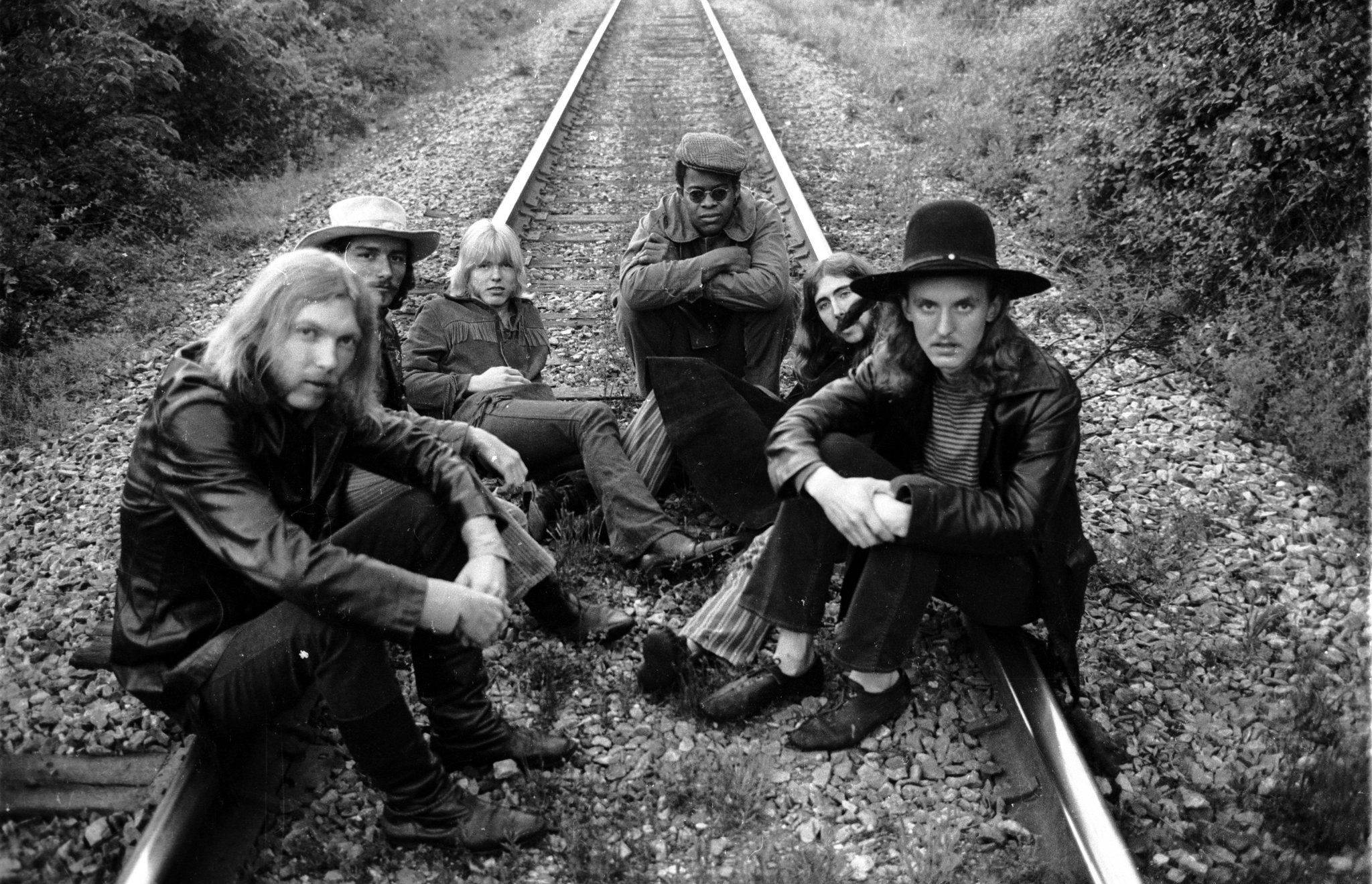 Allman Brothers Band《Filmore West 71》 壁紙 — 六名身穿1970年代服裝的男子坐在和蹲在鐵路軌道上，兩旁是茂密的樹葉，一張清晰的黑白照片。
