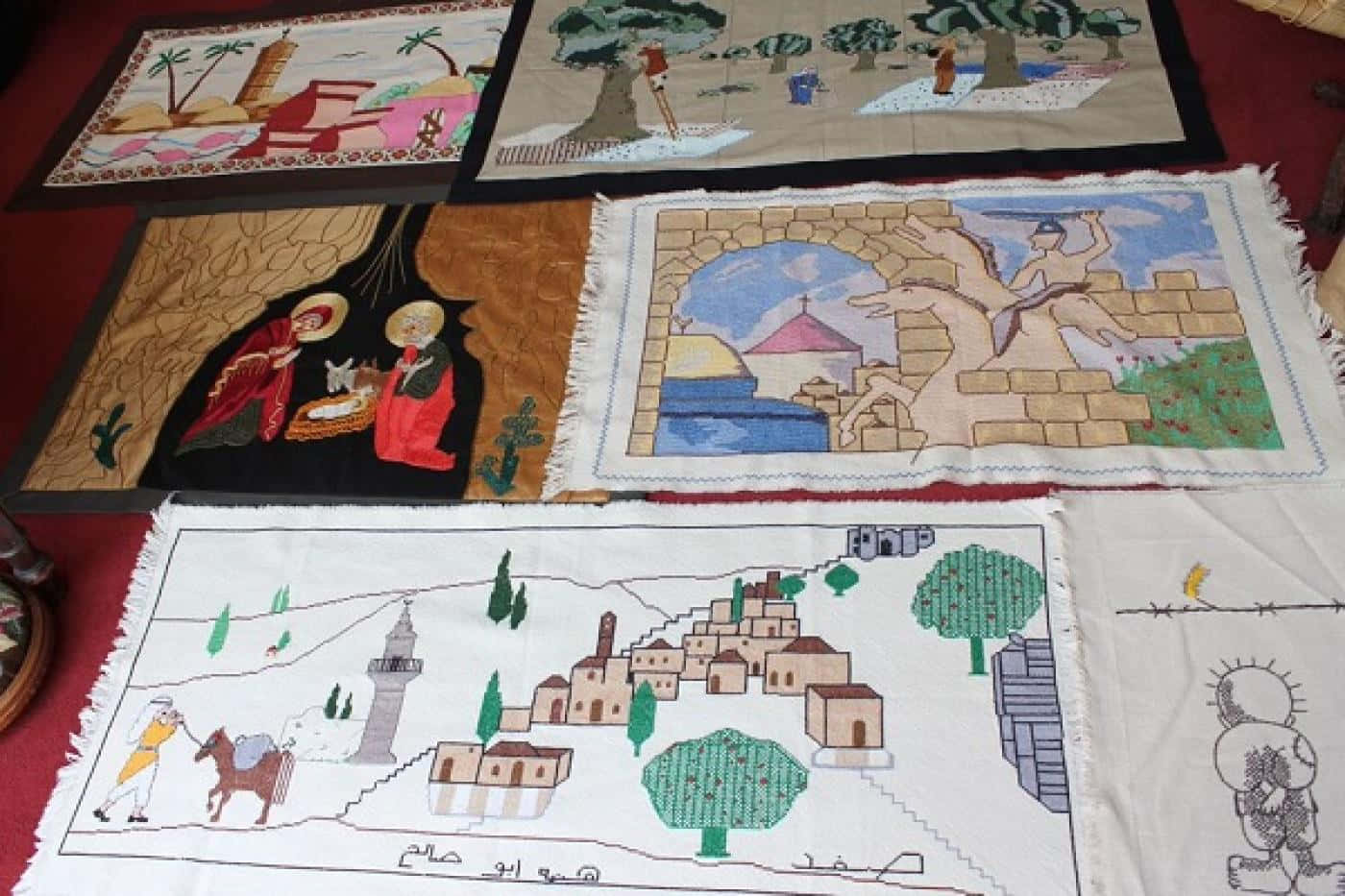 Palestine 桌布 壁紙 — 六塊刺繡紡織面板描繪聖經和文化場景，色彩鮮豔，邊緣帶流蘇，鋪在紅色表面上。