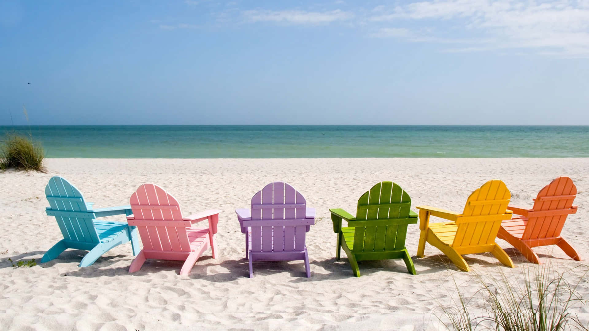 Beach Holiday 桌布 壁紙 — 六張色彩鮮豔的Adirondack椅子整齊排列在純淨的白色沙灘上，面向平靜的藍綠色海洋，上方是清澈的藍天。