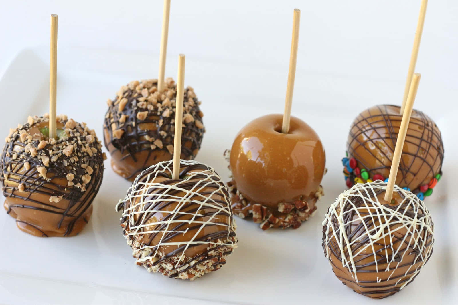Caramel Apples 桌布 壁紙 — 六款美食焦糖蘋果，配以堅果、朱古力醬和彩色糖果等各式配料，整齊排列在白色碟子上。