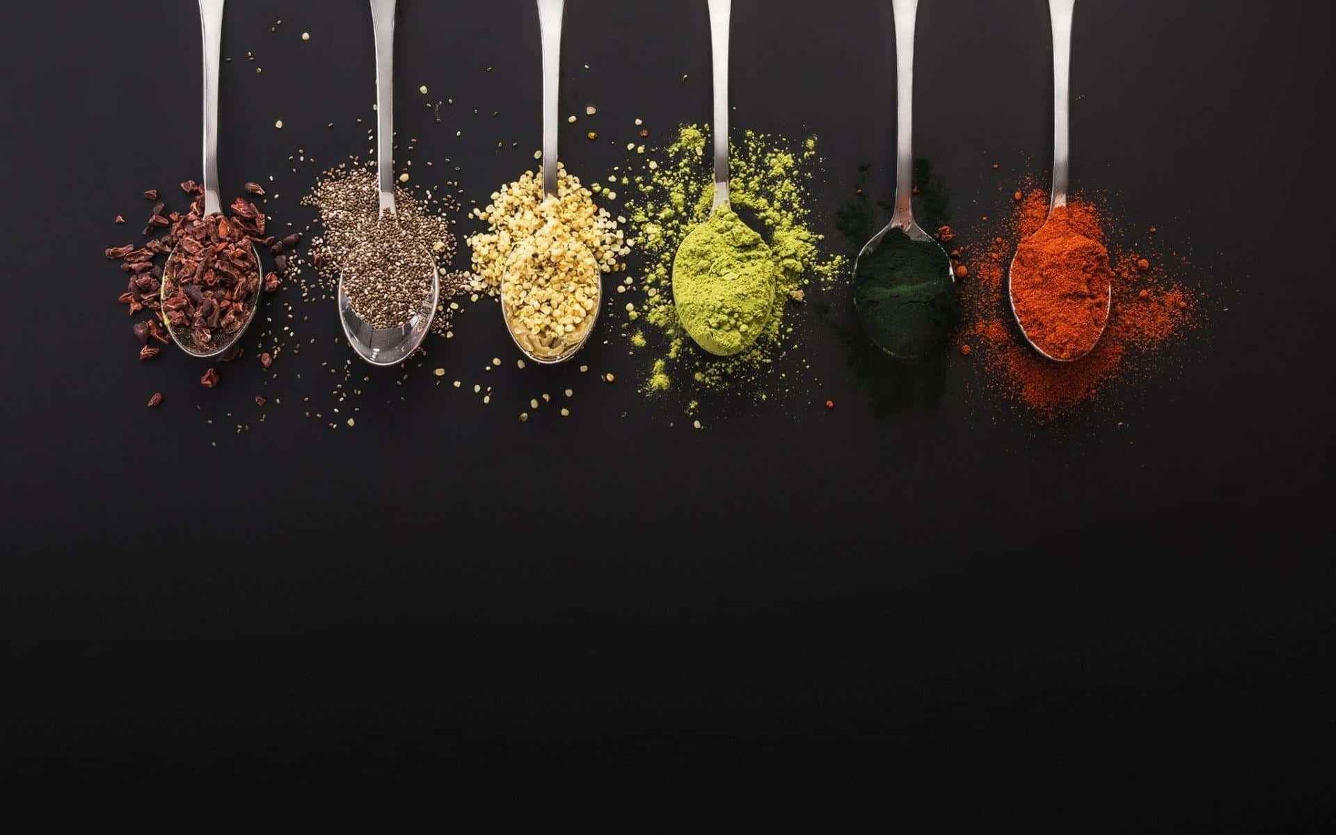 Spices 桌布 壁紙 — 六隻湯匙盛載著鮮豔的香料，背景是純黑色，並有散落的粉末。