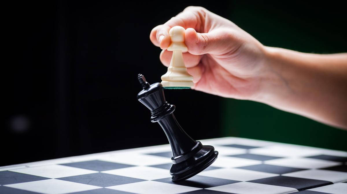 兵棋小兵擊敗國王 壁紙 — 一隻手在深色背景的棋盤上將白色棋子舉起在倒下的黑色國王之上。