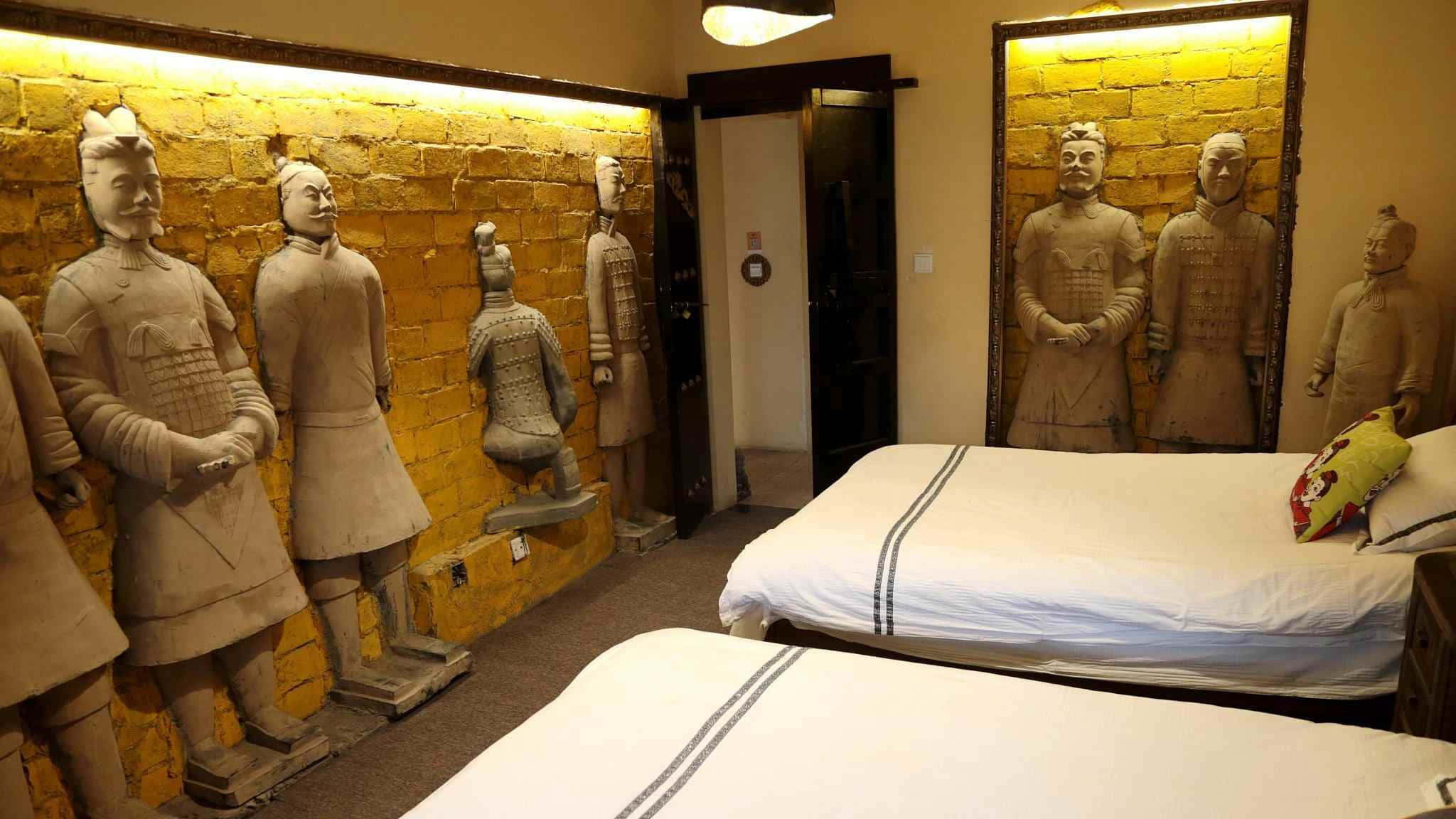 兵馬俑雕塑裝飾的房間 壁紙 — 一間酒店房間，黃色磚牆上安裝了兵馬俑雕像，旁邊有兩張床。