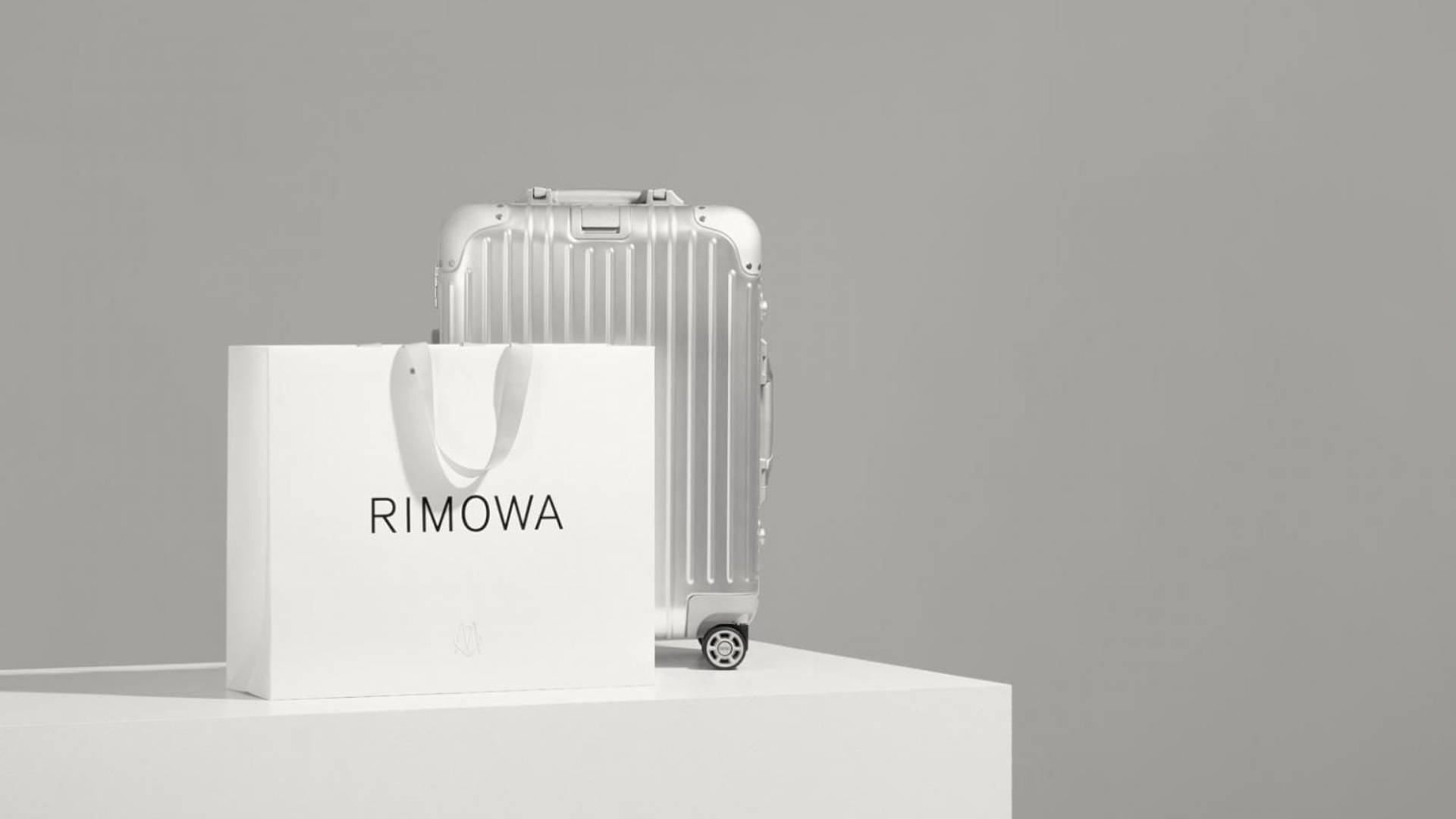 銀色Rimowa行李箱和品牌紙袋放在白色底座上。