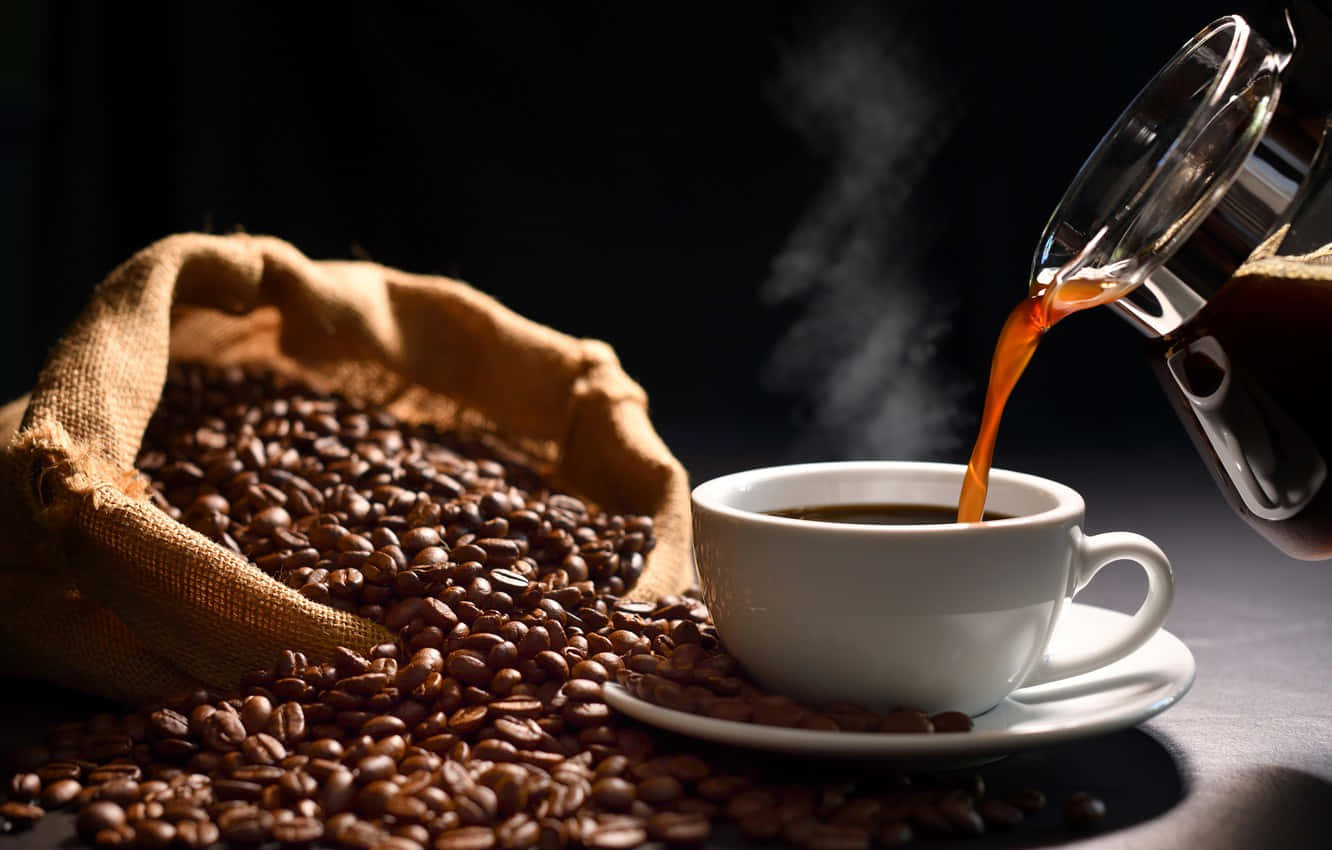 Brown Coffee 桌布 壁紙 — 冒煙的咖啡從玻璃壺倒入白色杯子，旁邊是一個裝滿烘焙咖啡豆的麻布袋。