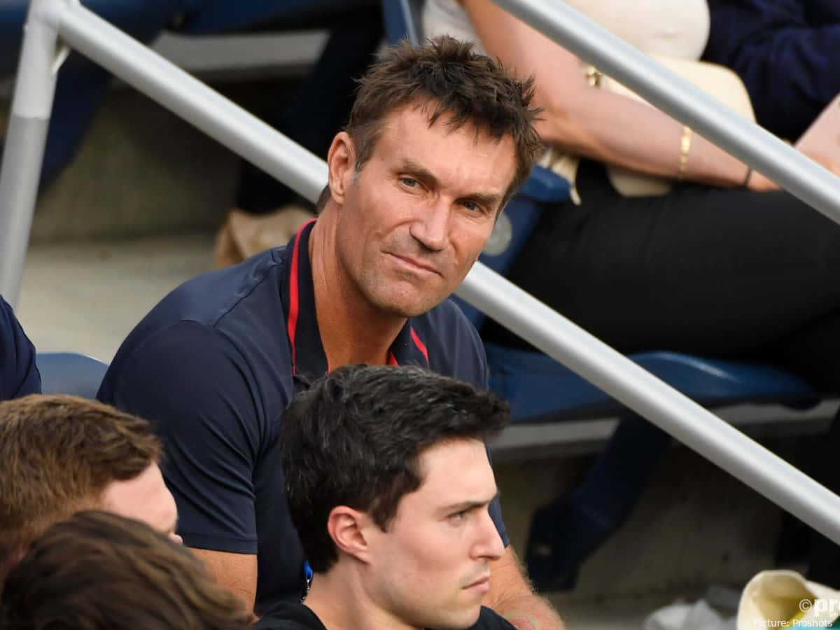 冠軍 Pat Cash 壁紙 — 一個頭髮凌亂、表情嚴肅的男人坐在體育館看台上，專注地向前看。