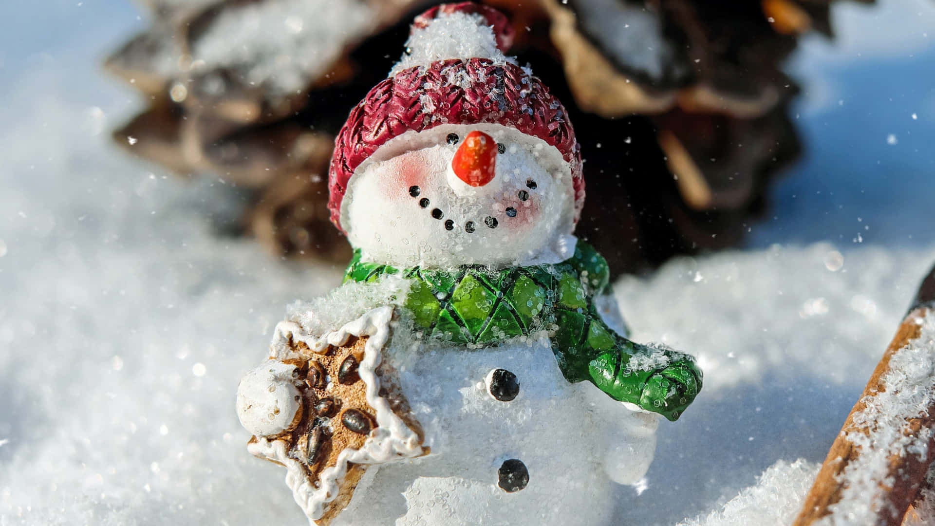 冬季仙境 壁紙 — 一個快樂的雪人公仔，戴著紅帽子和綠色圍巾，在雪白的冬日場景中拿著一顆星形曲奇。