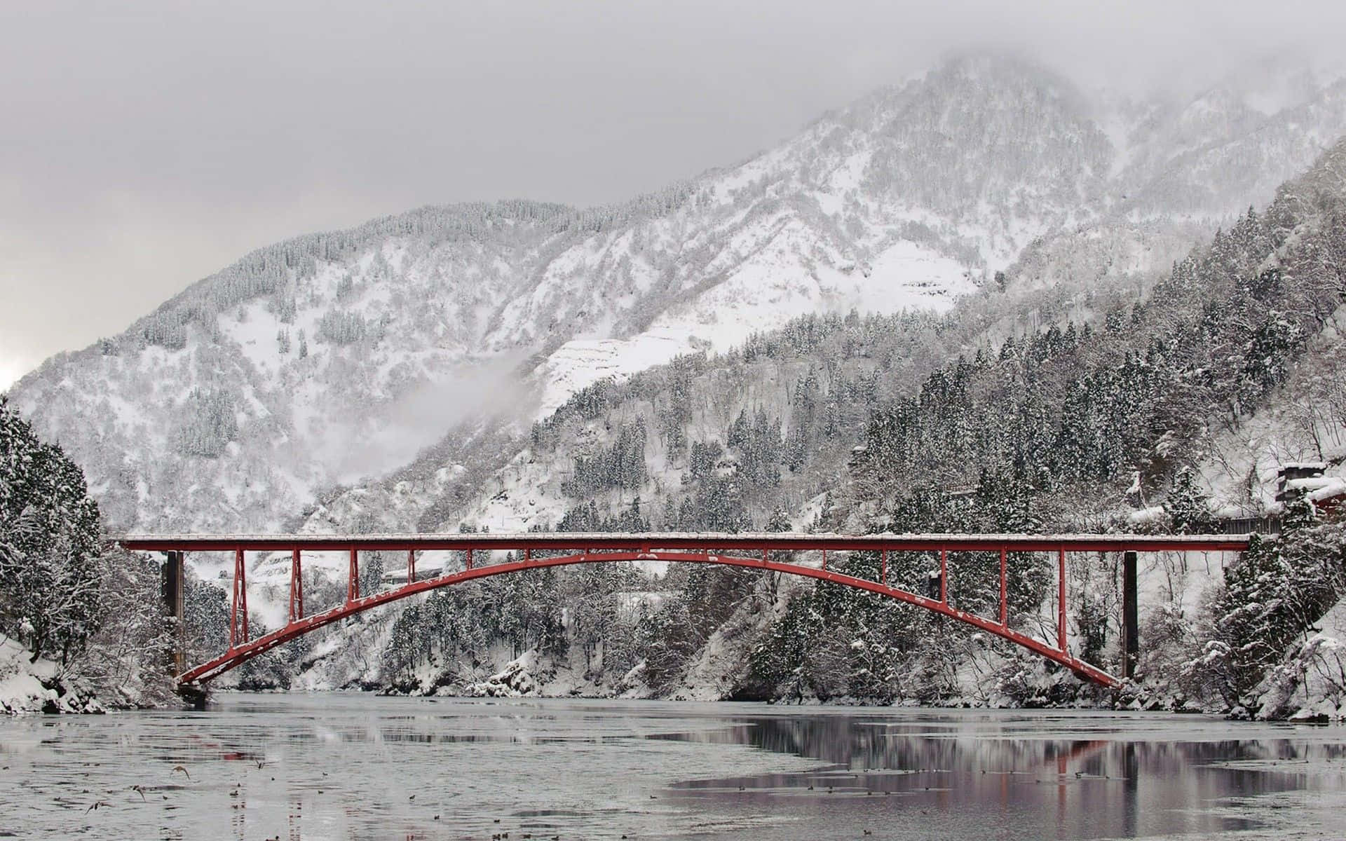雪景山區中，紅色拱橋橫跨結冰的河流。