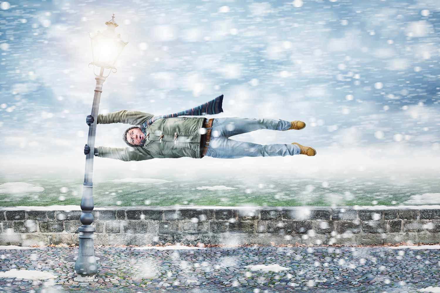 冬季仙境中的晶瑩暴雪 壁紙 — 一個男人水平漂浮，抓住一個沾滿雪的燈柱，背景是雪景城市和飄落的雪花。