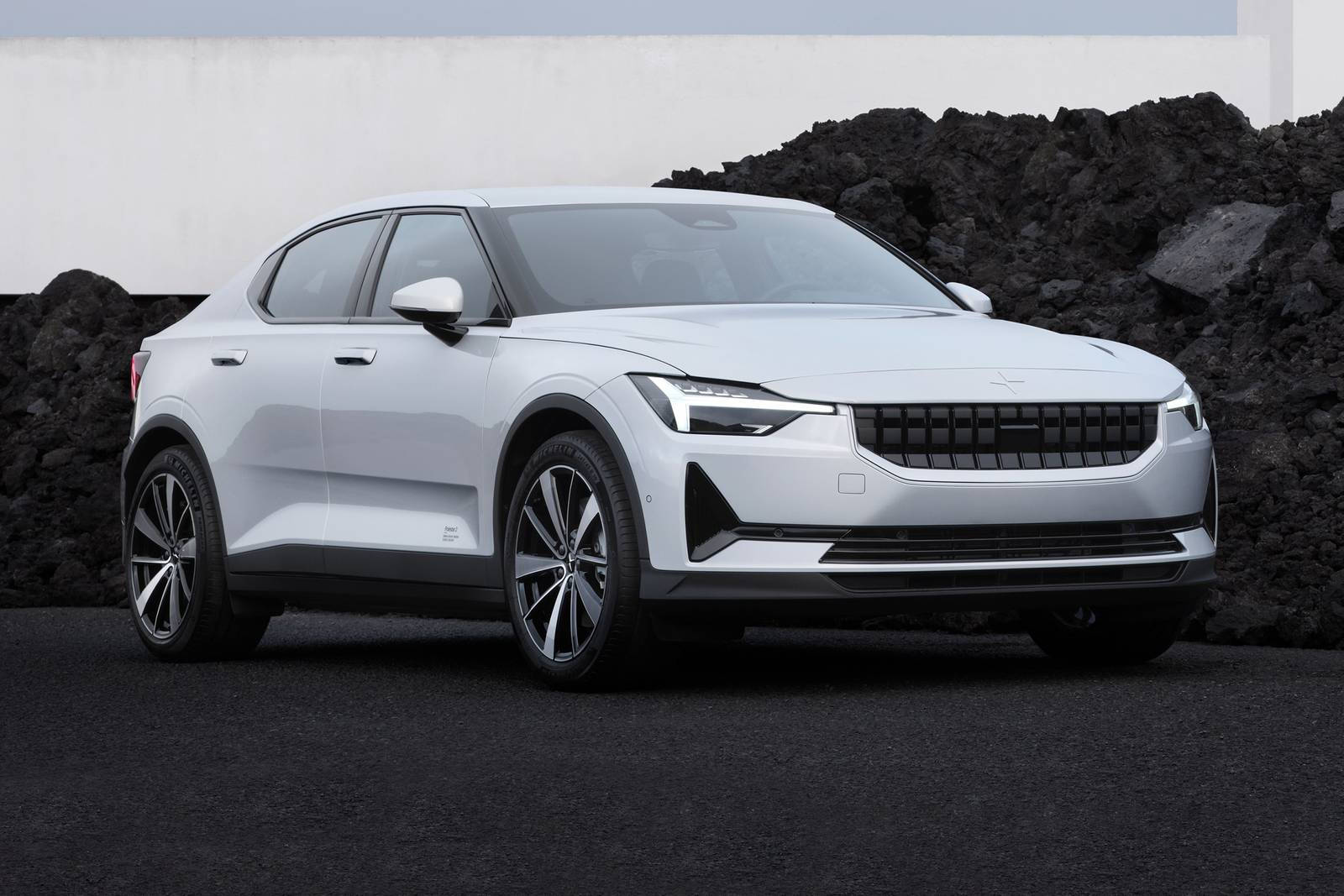 冬季冒險與 Polestar 混合動力車 壁紙 — 一輛線條銳利、帶黑色點綴的時尚白色電動車，在黑色火山岩和極簡白牆的簡樸背景下蓄勢待發。