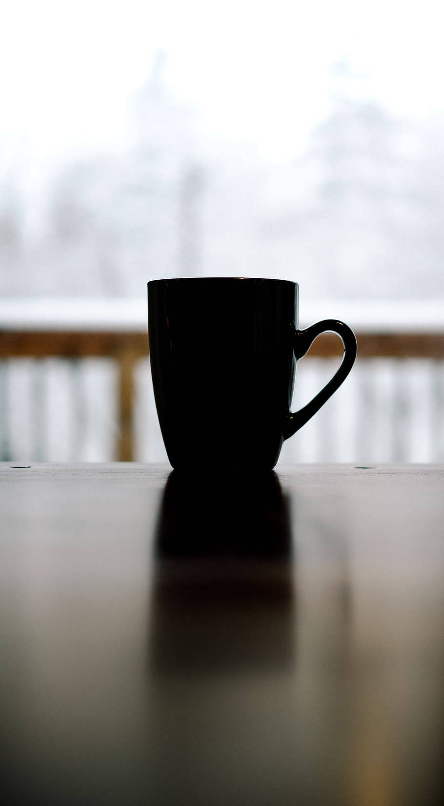 冬季咖啡杯 壁紙 — 一個黑色咖啡杯放在木桌上，背景是模糊的雪景。