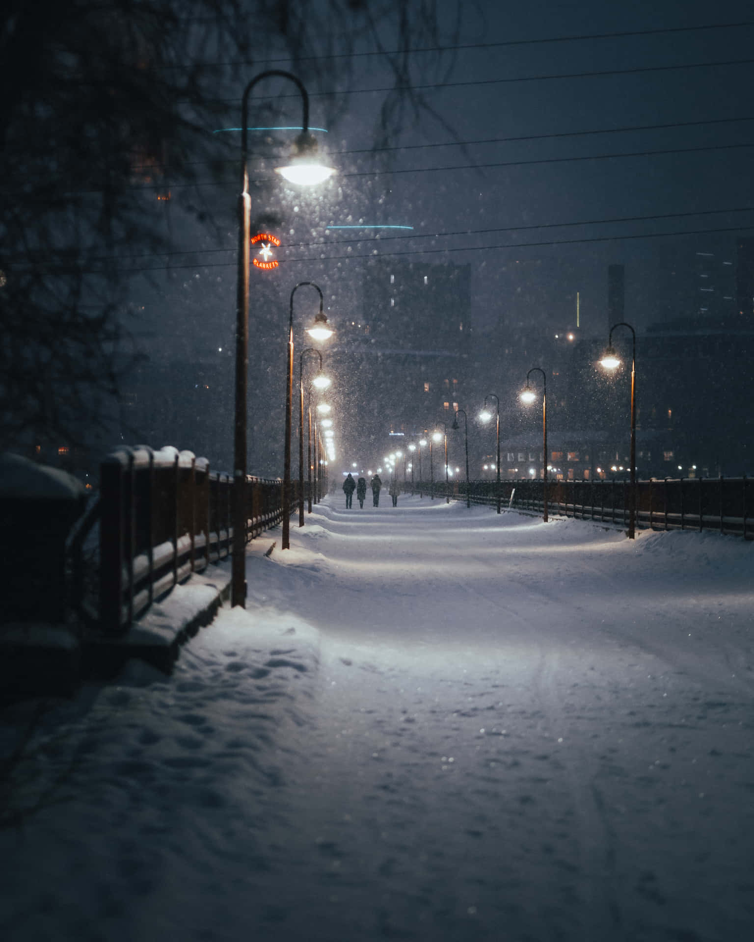 夜間被街燈照亮的積雪城市步道，遠處有人行走。