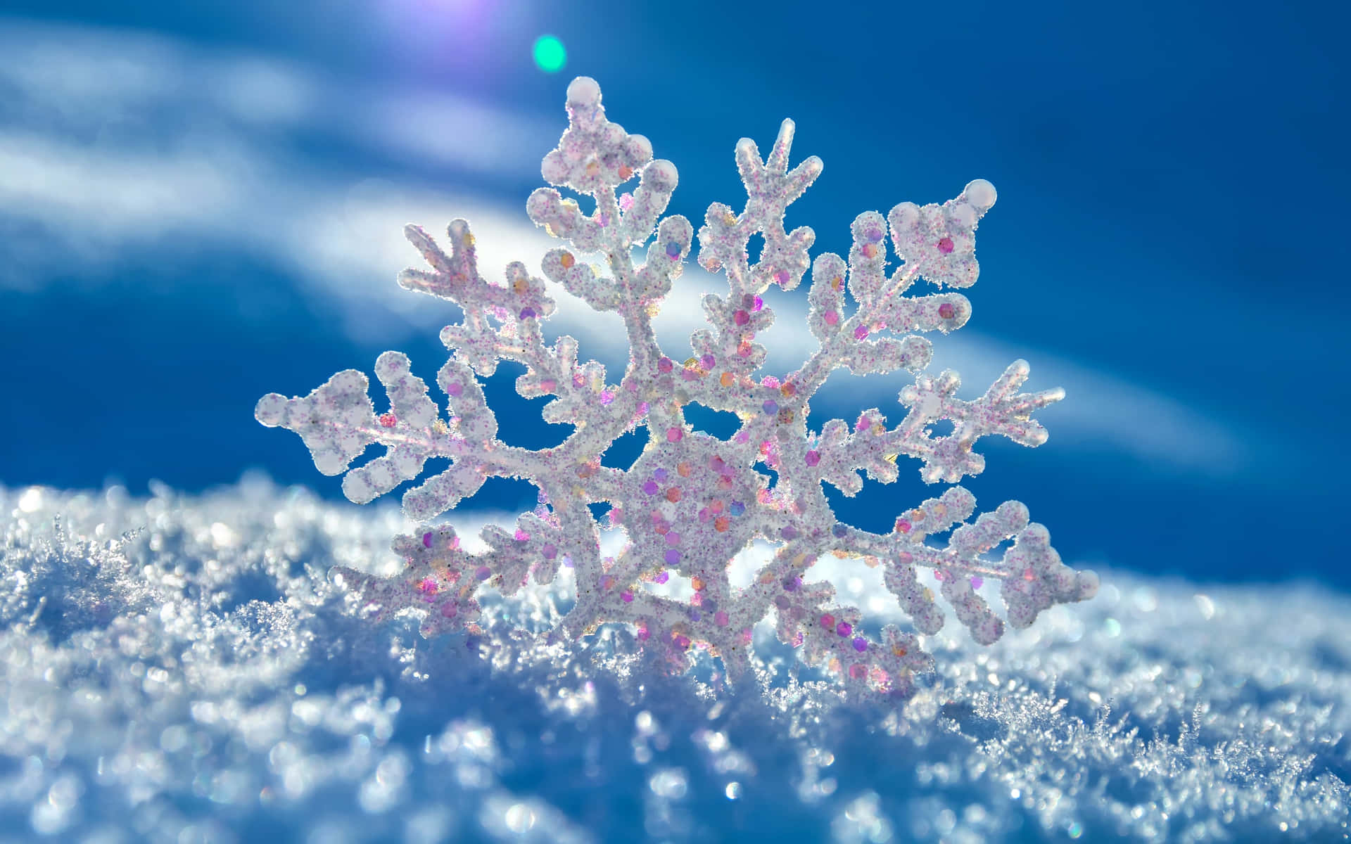 一片細節豐富的雪花，帶有粉紅色閃粉，躺在明亮的藍天下雪地上。