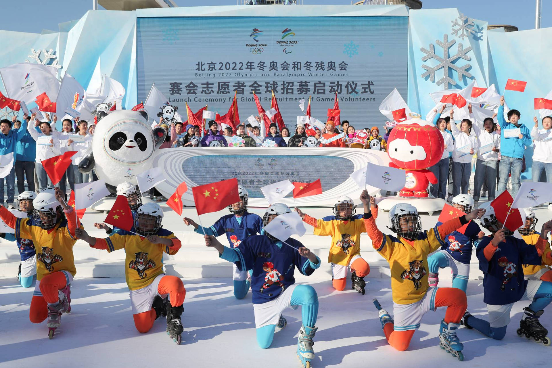 孩子們穿著滾軸溜冰鞋揮舞中國國旗，旁邊是奧運吉祥物，在冬季運動會活動中。