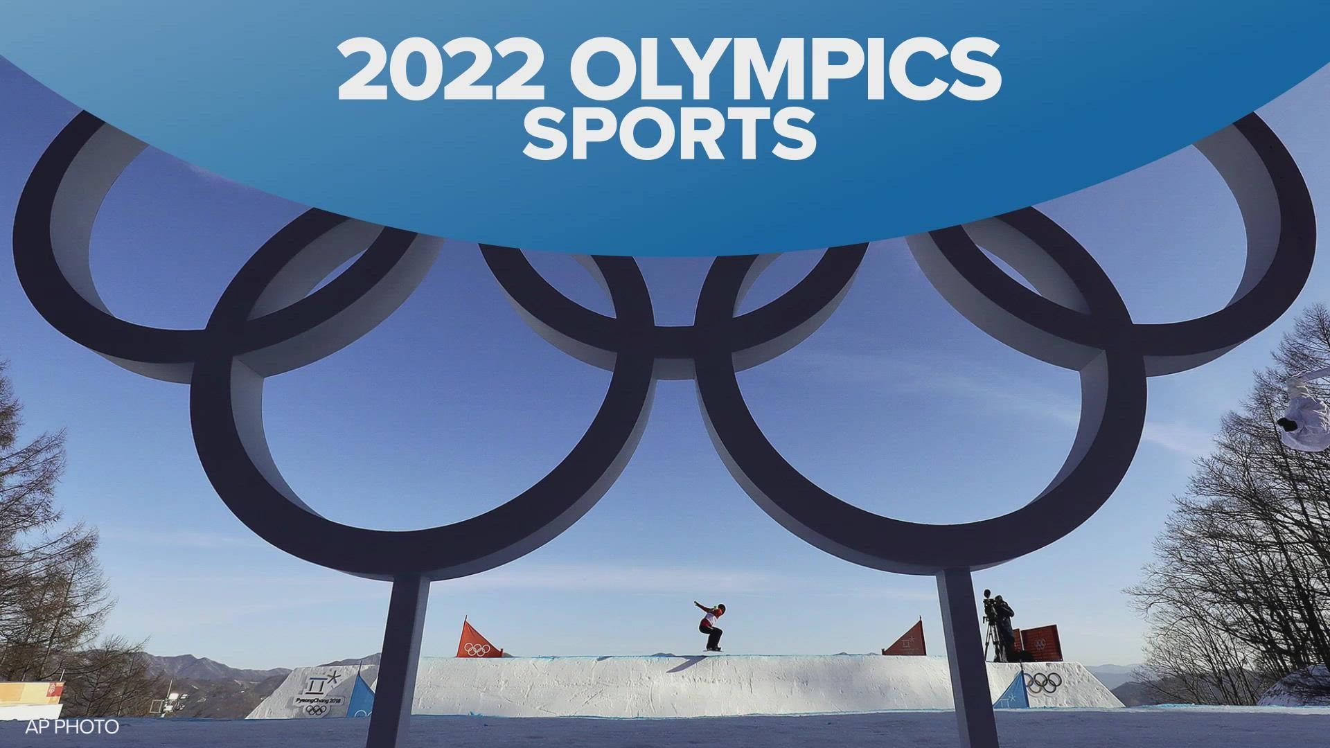 冬季奧運雪坡上的高速衝刺 壁紙 — 一名滑雪板運動員在2022年冬奧會的巨大奧運五環下翱翔，背景是晴朗的藍天。