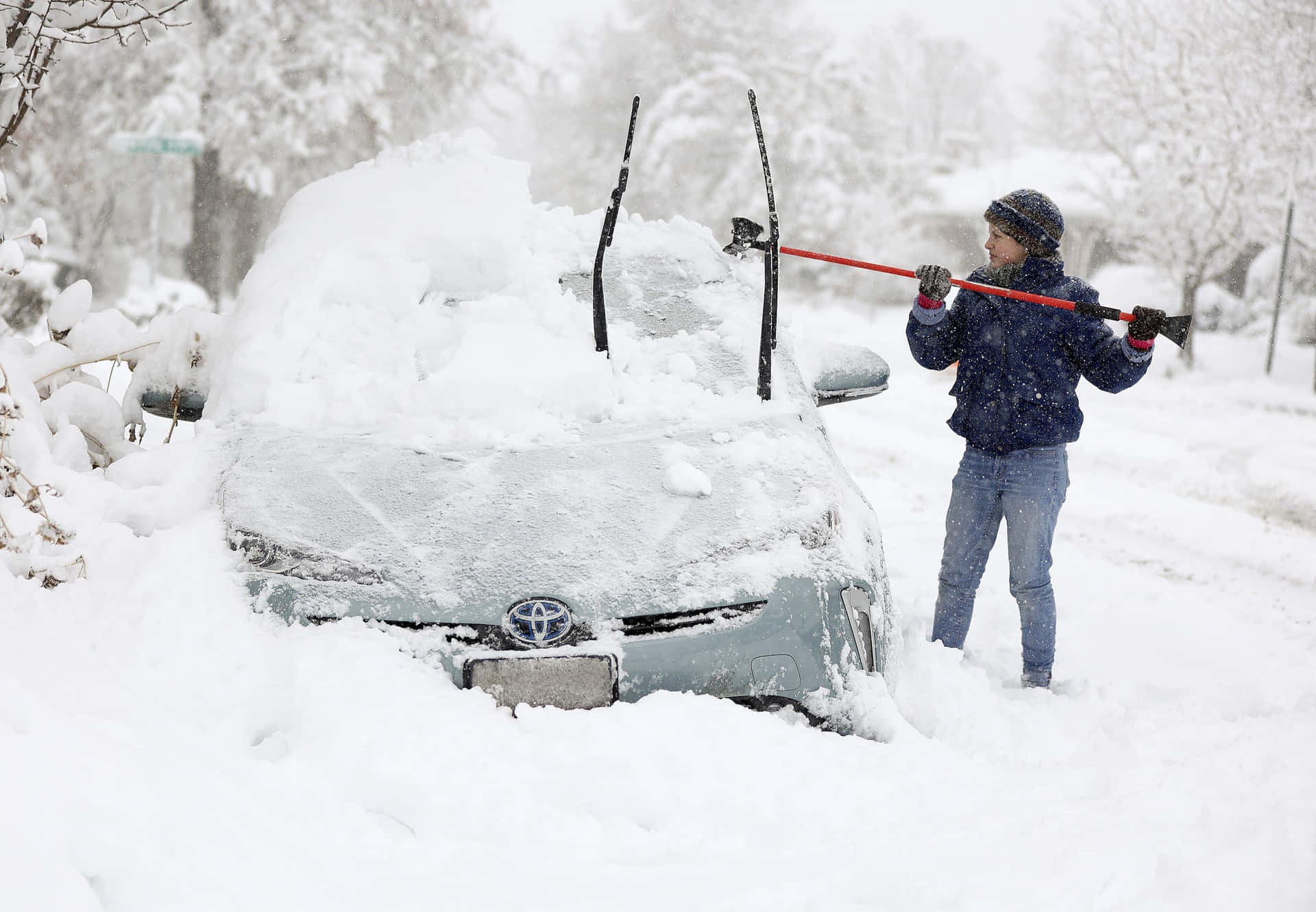 在大雪中從汽車上剷雪的人。