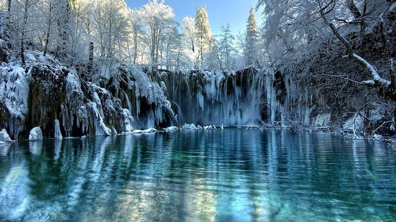 冰凍瀑布，冰崖和白雪覆蓋的樹木倒映在綠松石色的水中。