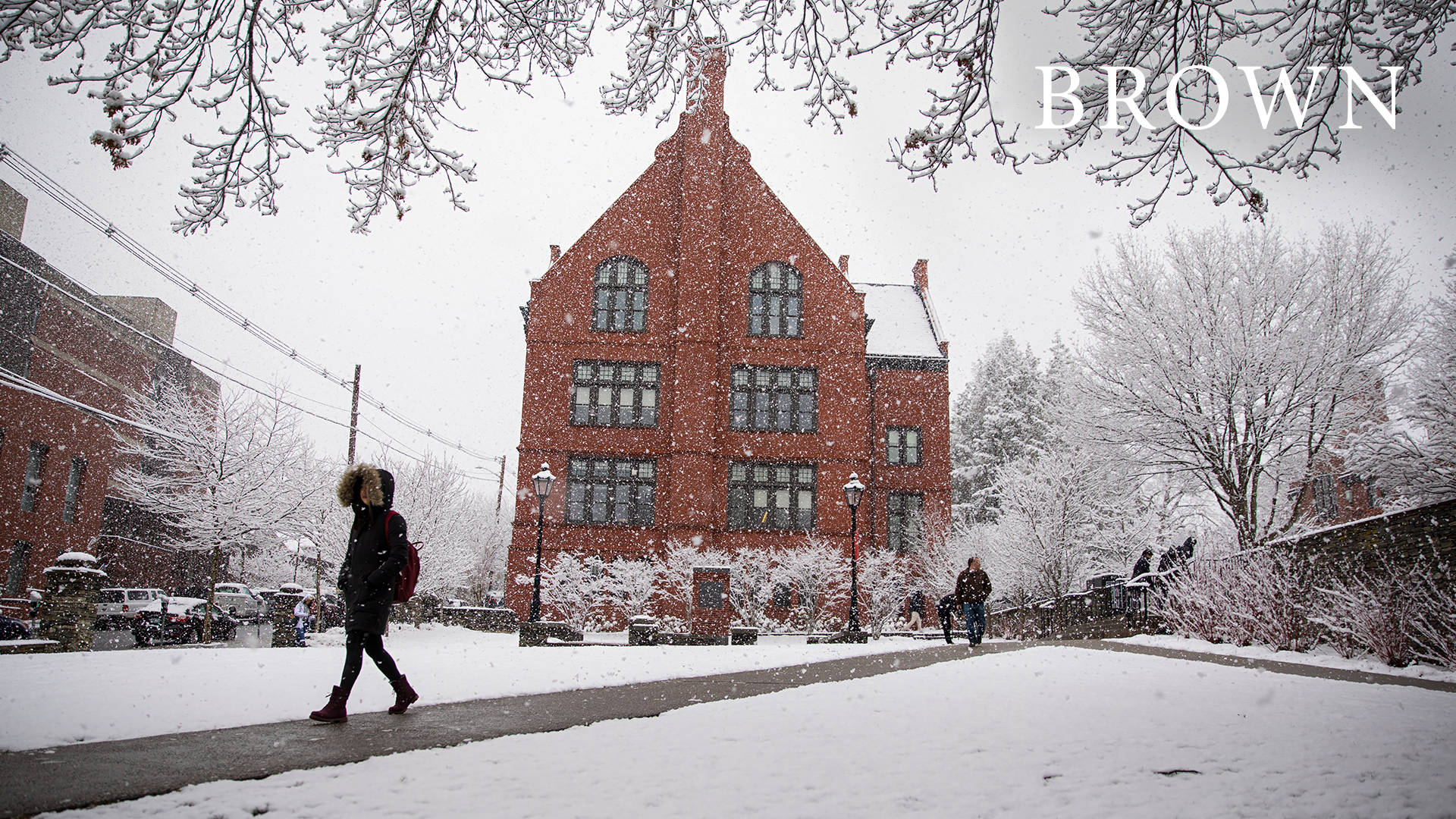 學生在積雪的校園小徑上行走，靠近磚造大學建築。