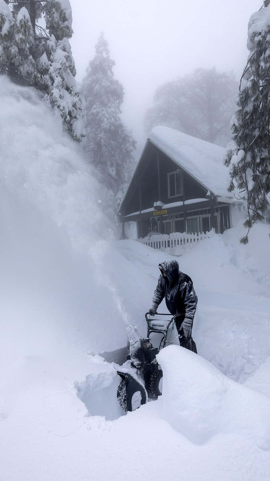 在雪地森林的小屋附近，用吹雪機清理積雪的人。
