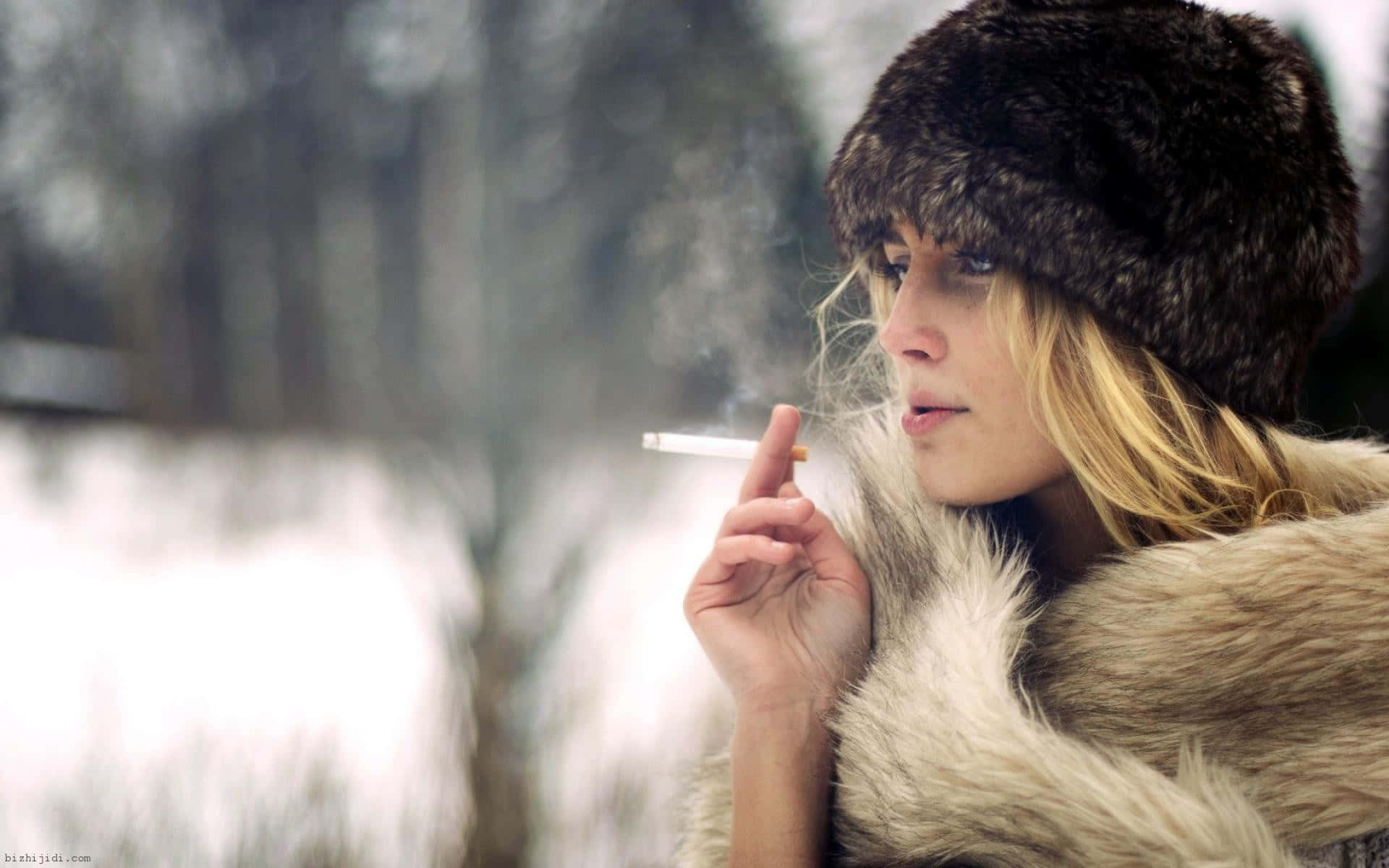 穿著毛大衣和帽子的女性在雪白的冬日場景中抽煙。