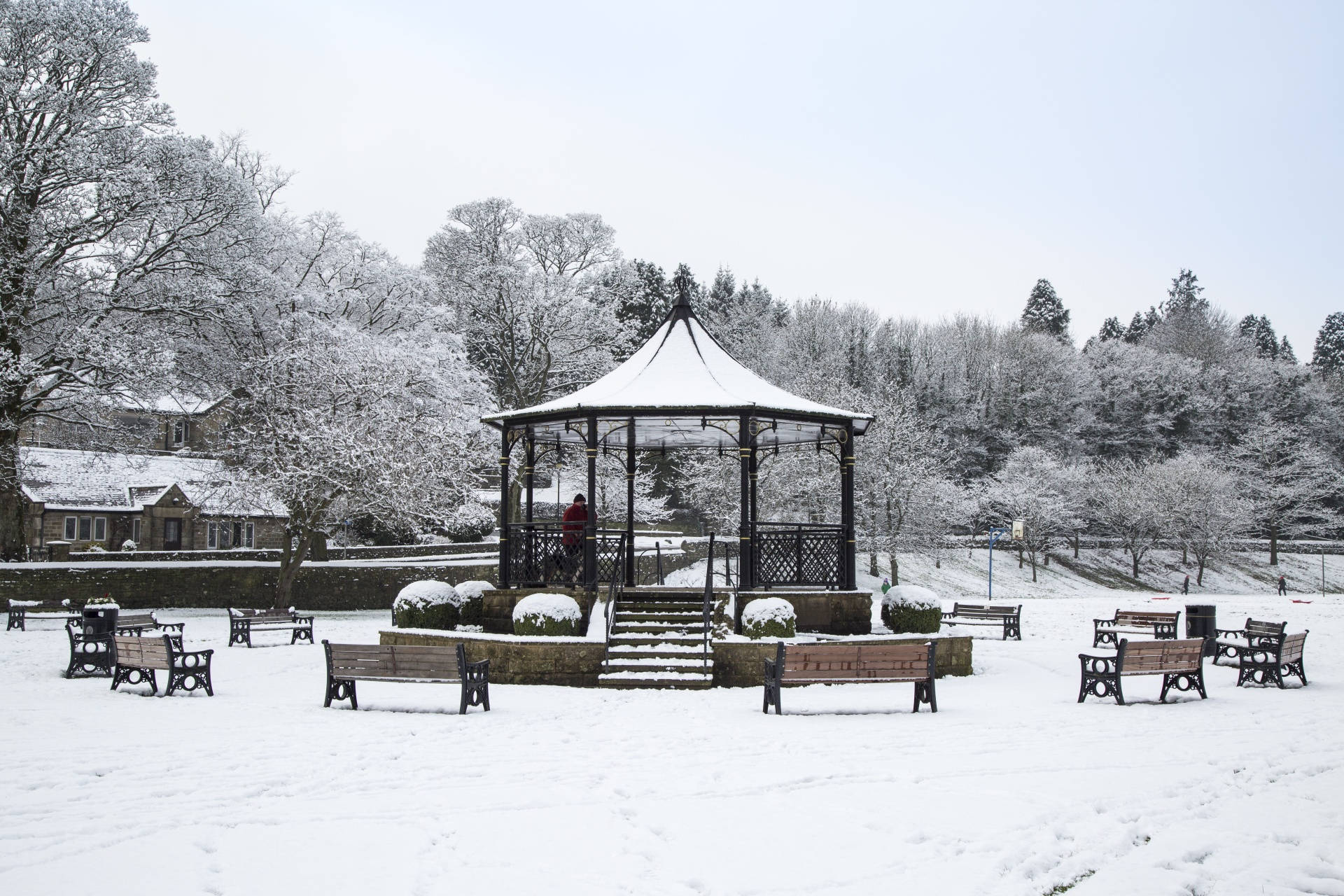 雪覆蓋了公園涼亭和長椅，在灰色的冬季天空下。