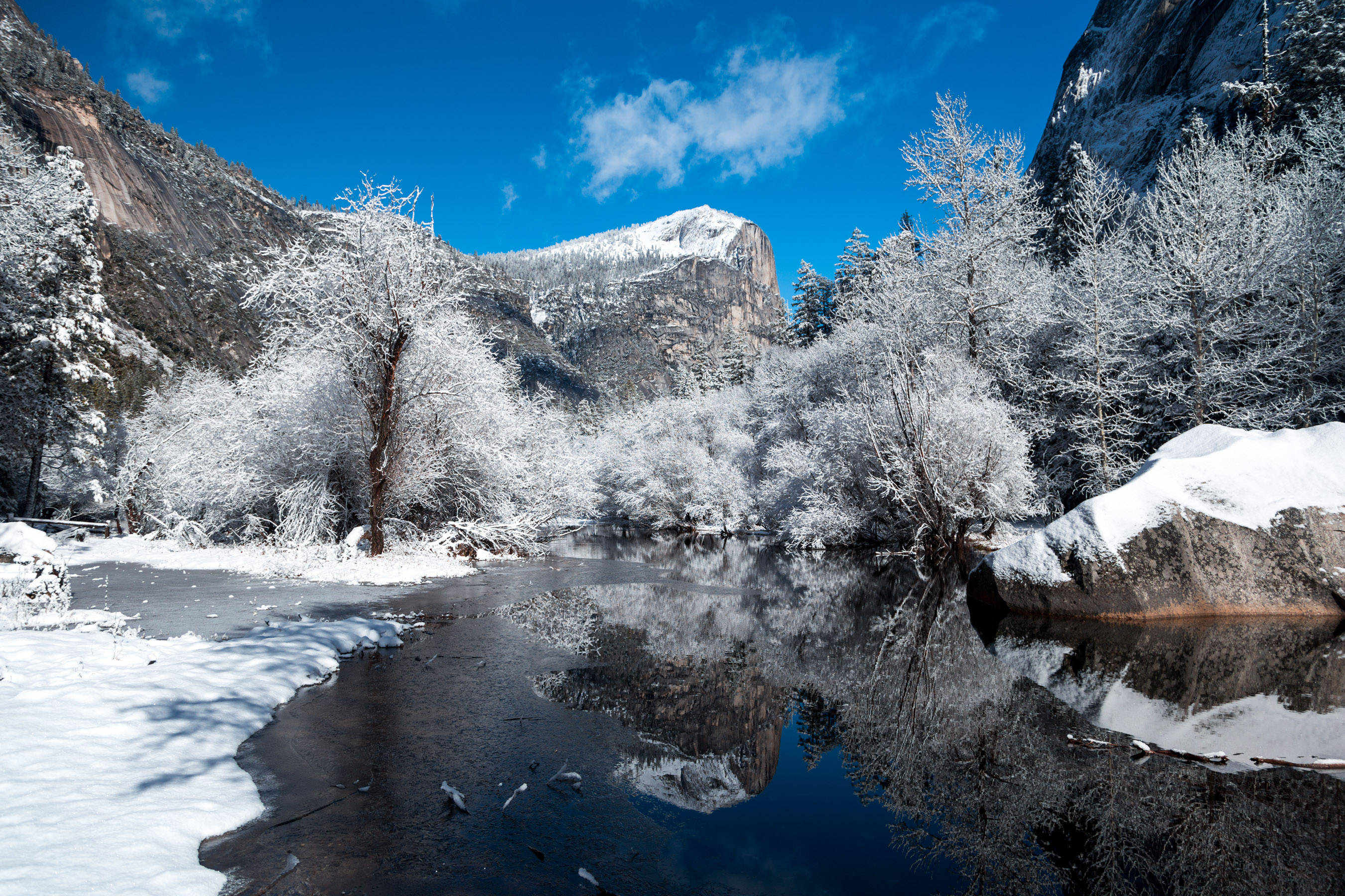 冬季美麗藍天 壁紙 — 白雪覆蓋著結霜的樹木和岩石，旁邊是一條平靜的河流，在明亮的藍天下映照著花崗岩懸崖。