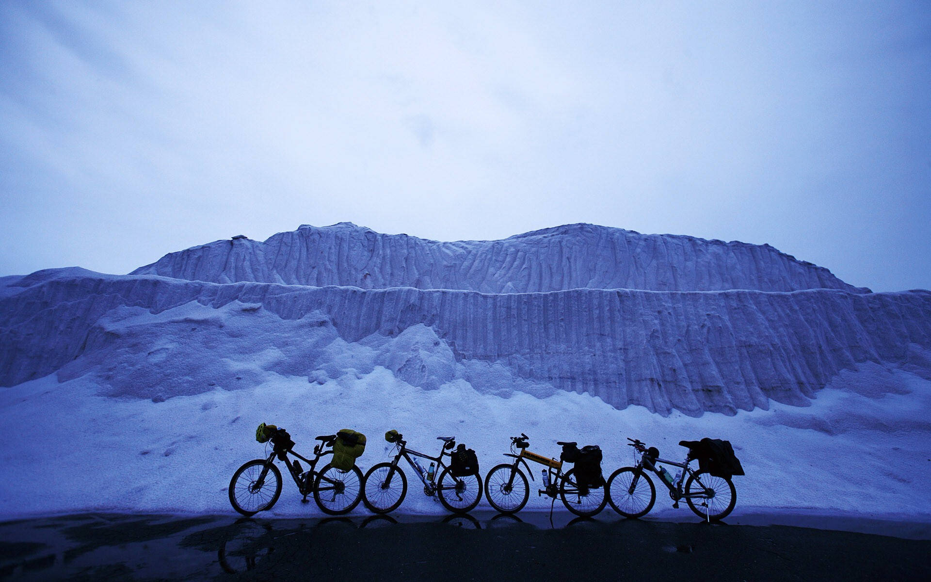 四輛旅行單車在暮色中停放在雪山前。