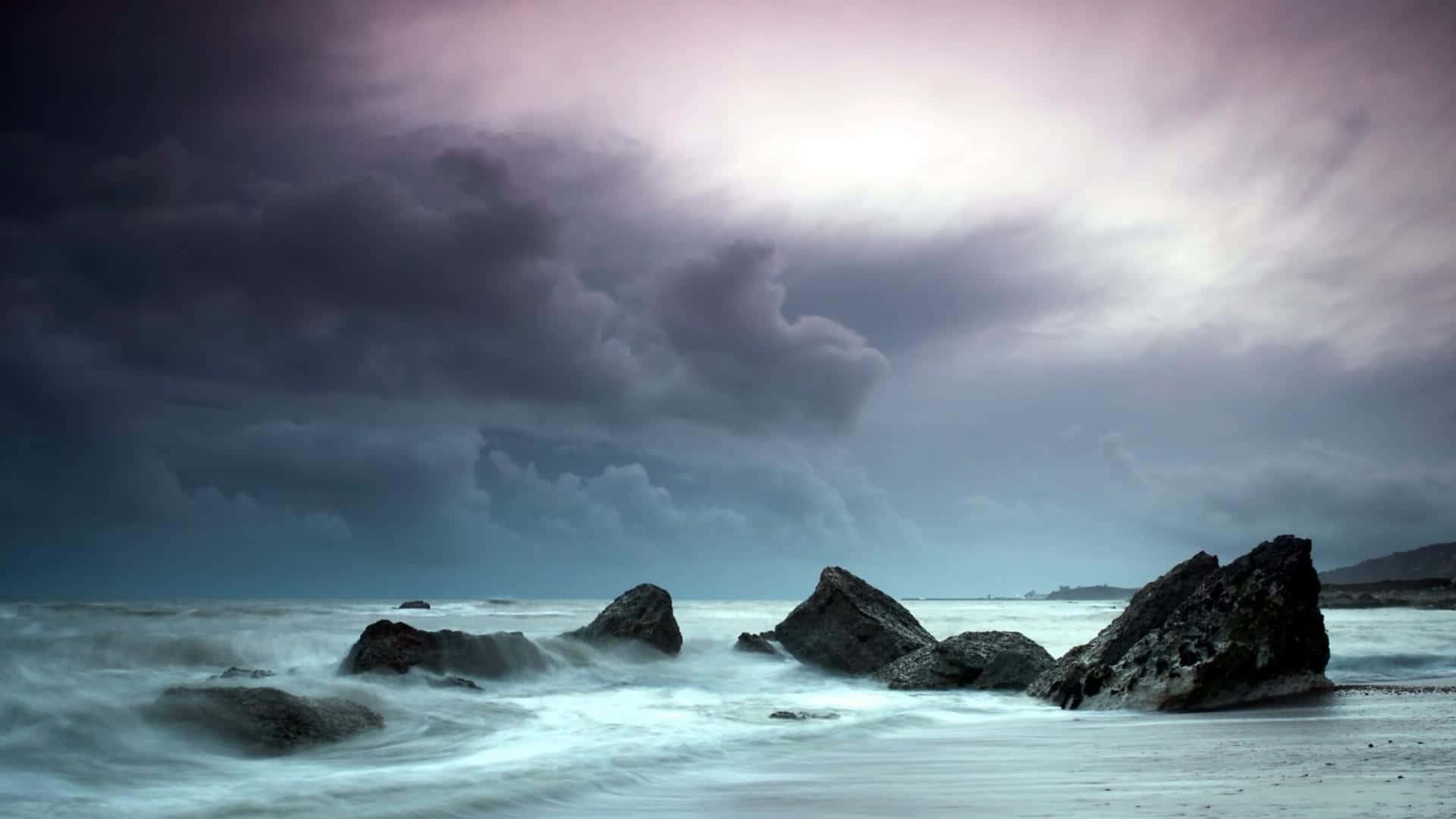 冬季陰鬱天空的寫真 壁紙 — 暴風雨的海浪拍打著崎嶇的岩石，天空呈現戲劇性的紫色和灰色。