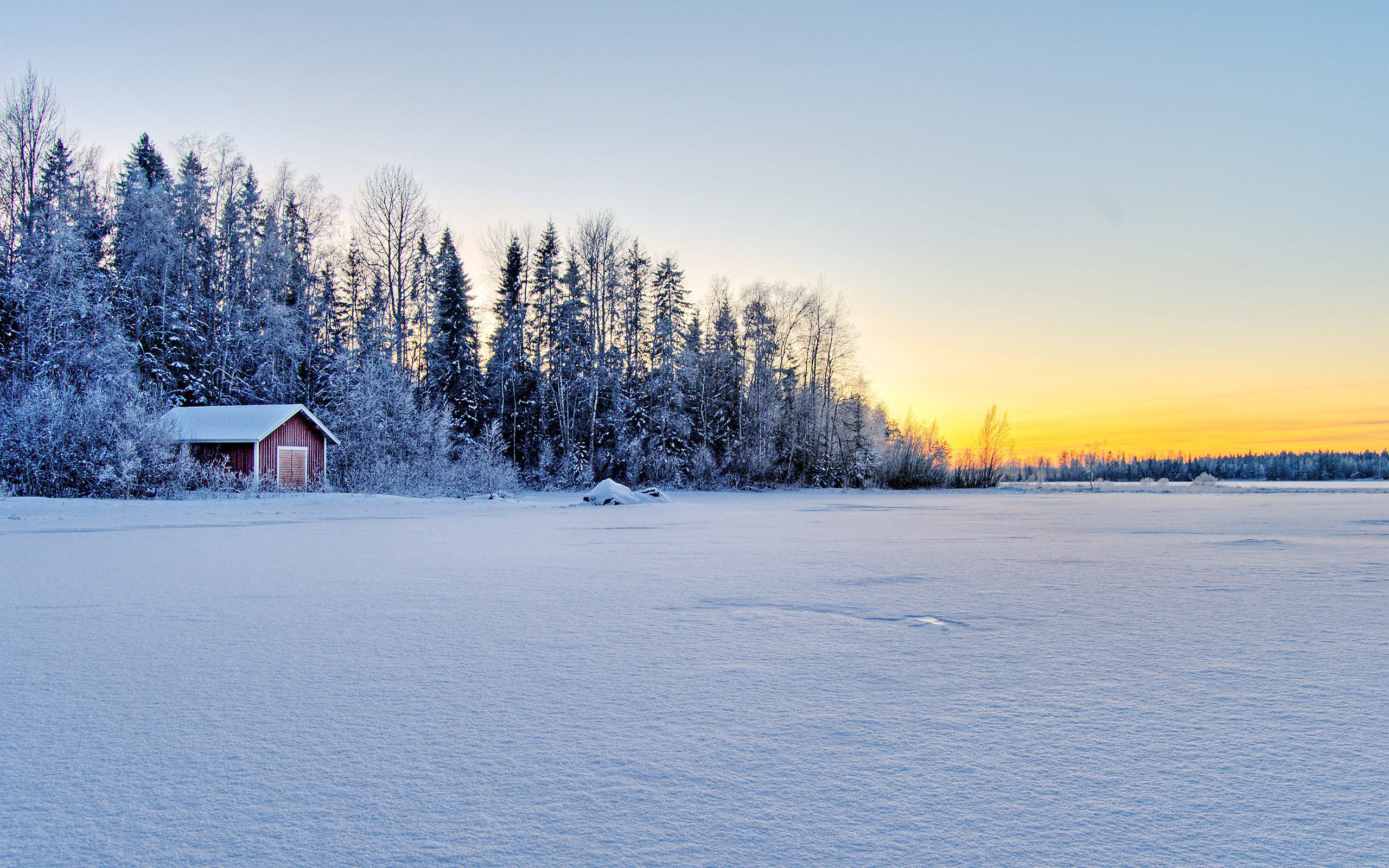 冬日冰湖風景 壁紙 — 一座孤獨的紅色小屋坐落在白雪覆蓋的樹林中，夕陽下冰湖延伸至發光的地平線。