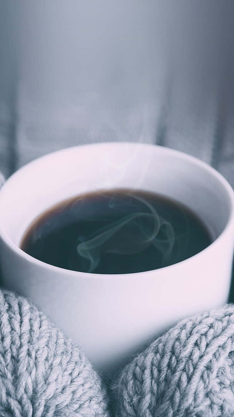 戴著針織手套的手握著一杯冒著蒸氣的咖啡。