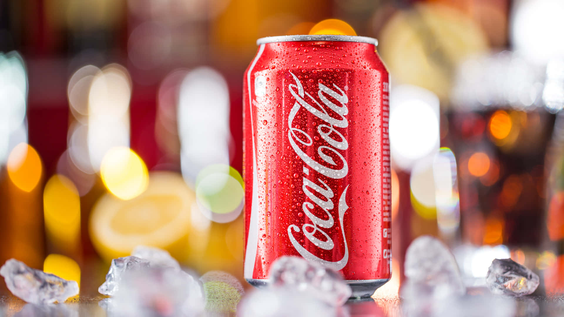 coca cola 桌布 壁紙 — 冰凍的可口可樂罐閃爍著冷凝水珠，被冰塊環繞，背景是溫暖模糊的酒吧。