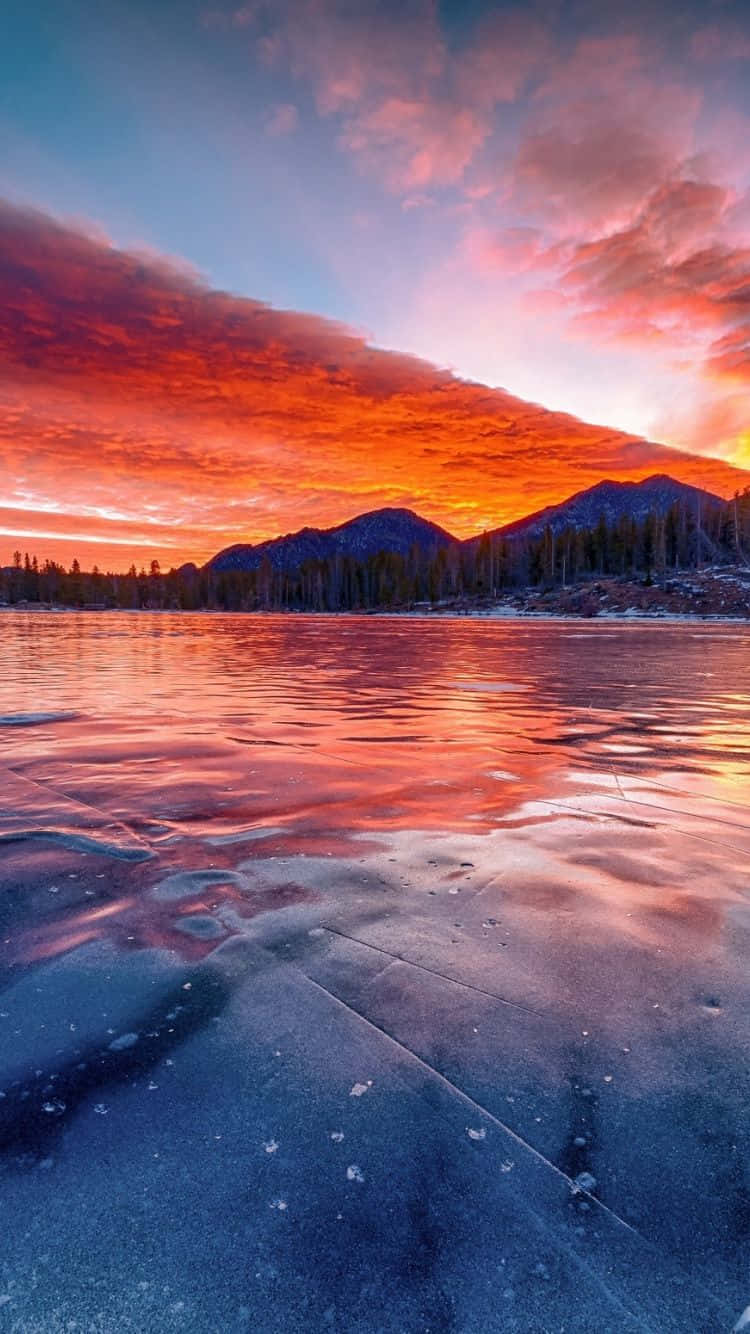 Frozen Lake 桌布 壁紙 — 冰凍的湖面映照著戲劇性天空下遠山上的熾熱日落。