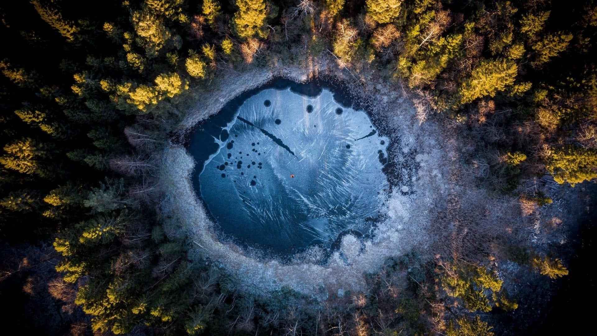 Frozen Lake 桌布 壁紙 — 冰封圓形湖的鳥瞰圖，周圍是茂密的森林，樹木呈現金黃秋色。