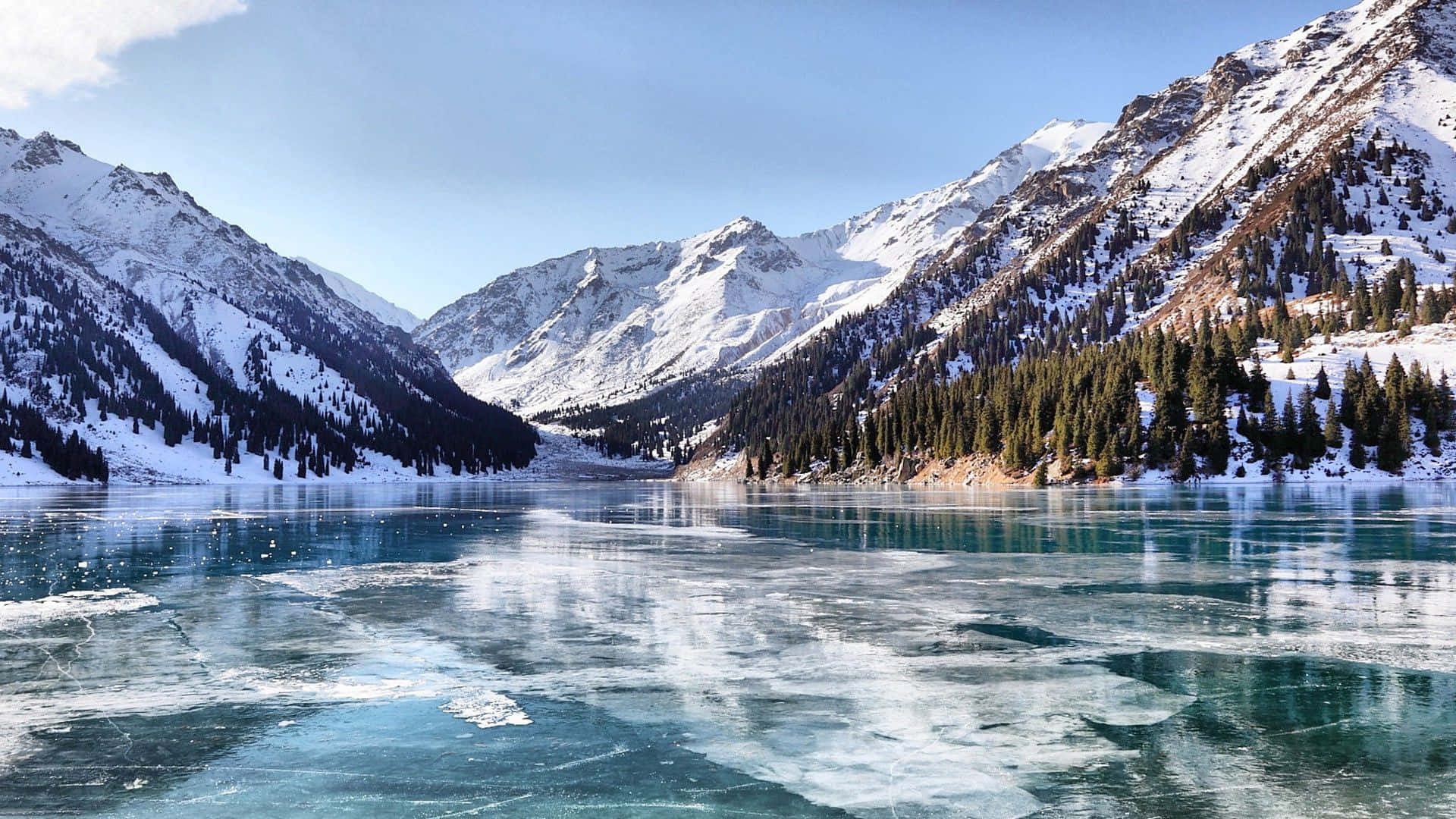 Frozen Lake 桌布 壁紙 — 冰封的藍綠色湖泊坐落在白雪覆蓋的山峰之間，天空清澈湛藍。