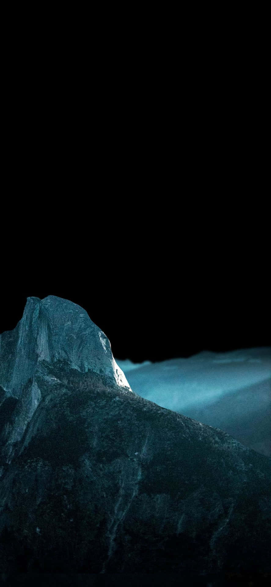 夜晚被藍光照亮的黑暗山峰，下方有霧。