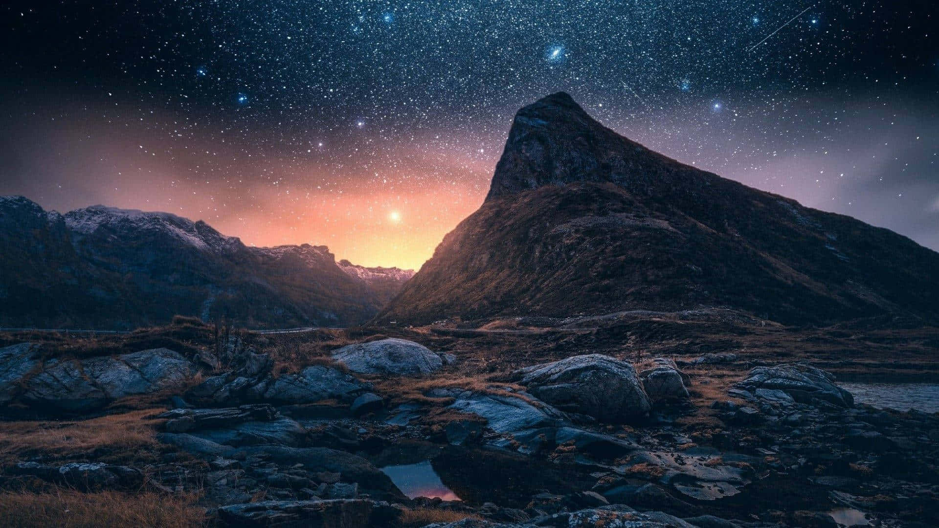 星空山景，日出在峰頂和前景岩石後方閃耀