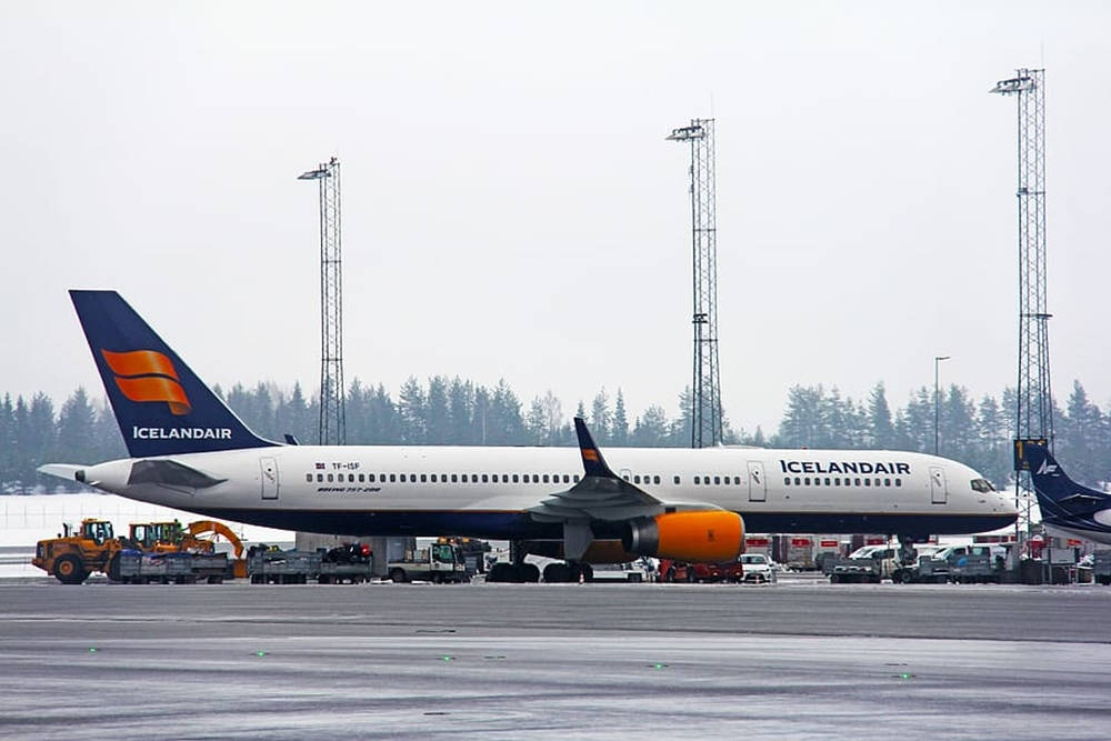 冰島航空飛機停泊在濕滑機場停機坪，背景有地勤車輛和樹林。