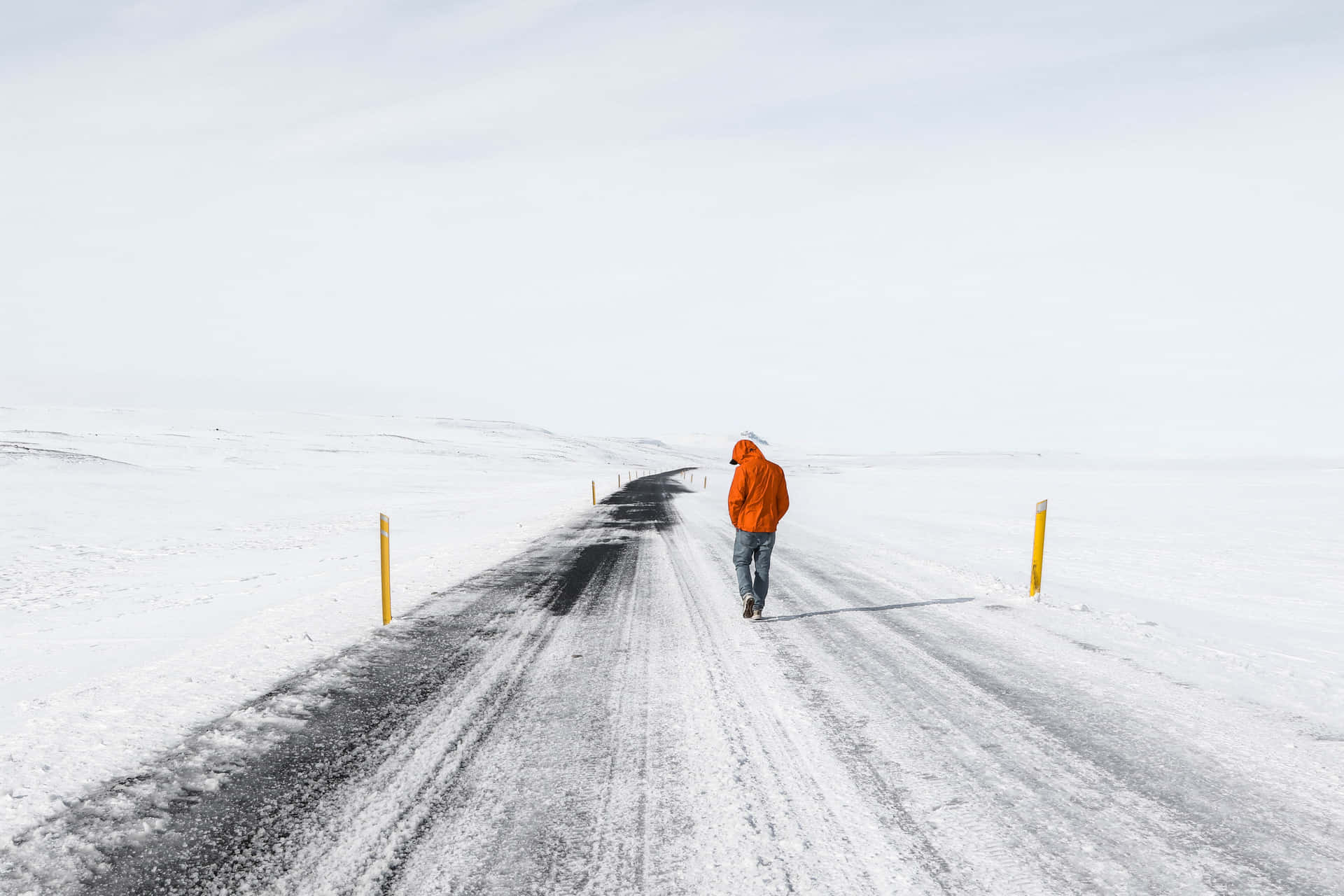 一個穿著橙色外套的人獨自走在廣闊冬季景觀中的雪路上。