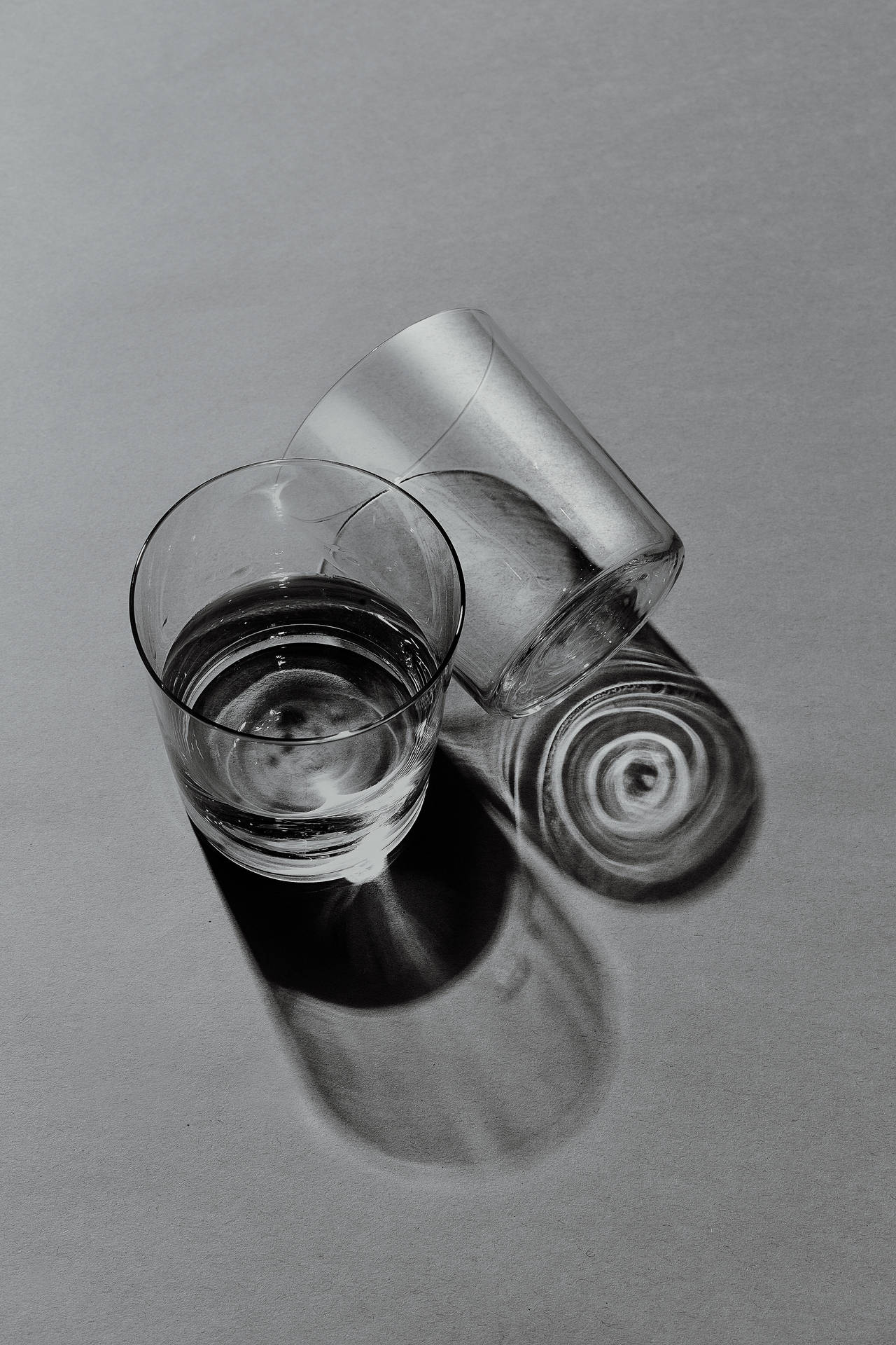 兩個玻璃杯，一個直立，一個傾倒，在灰色表面上投射陰影