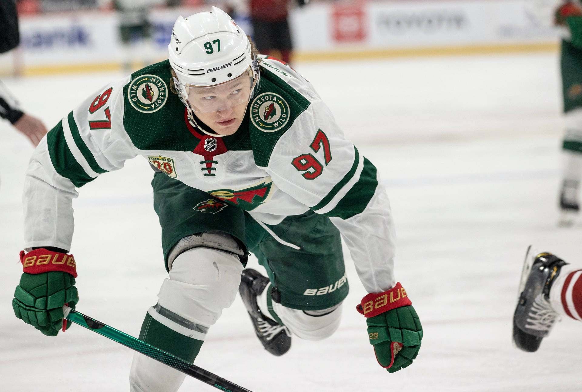 身穿綠色和白色球衣的曲棍球運動員在比賽期間在冰上滑行。