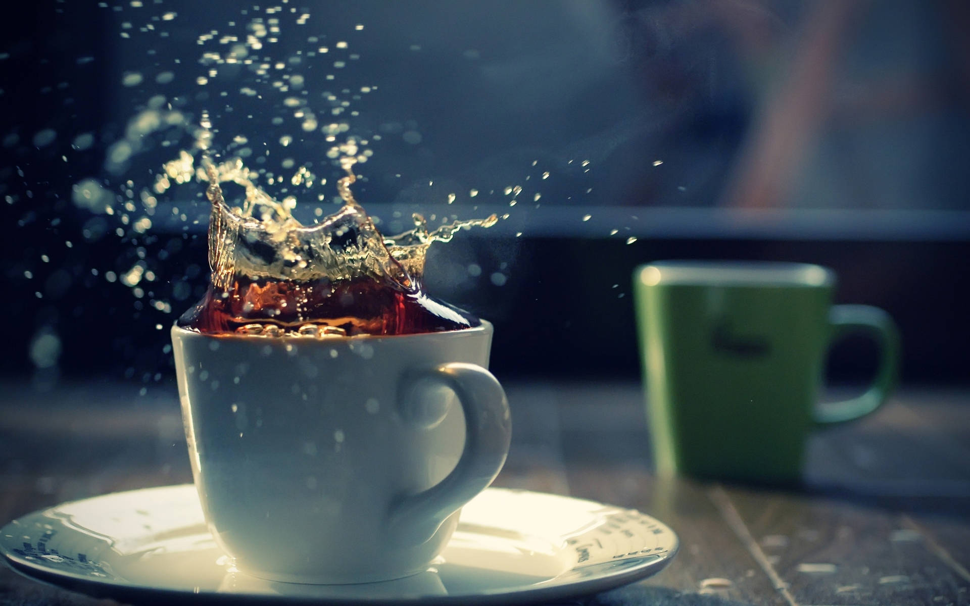 冰茶灑在白杯上 壁紙 — 一個裝著深色液體的白色杯子在模糊的深色背景上爆出金色飛濺，旁邊有一個綠色杯子。