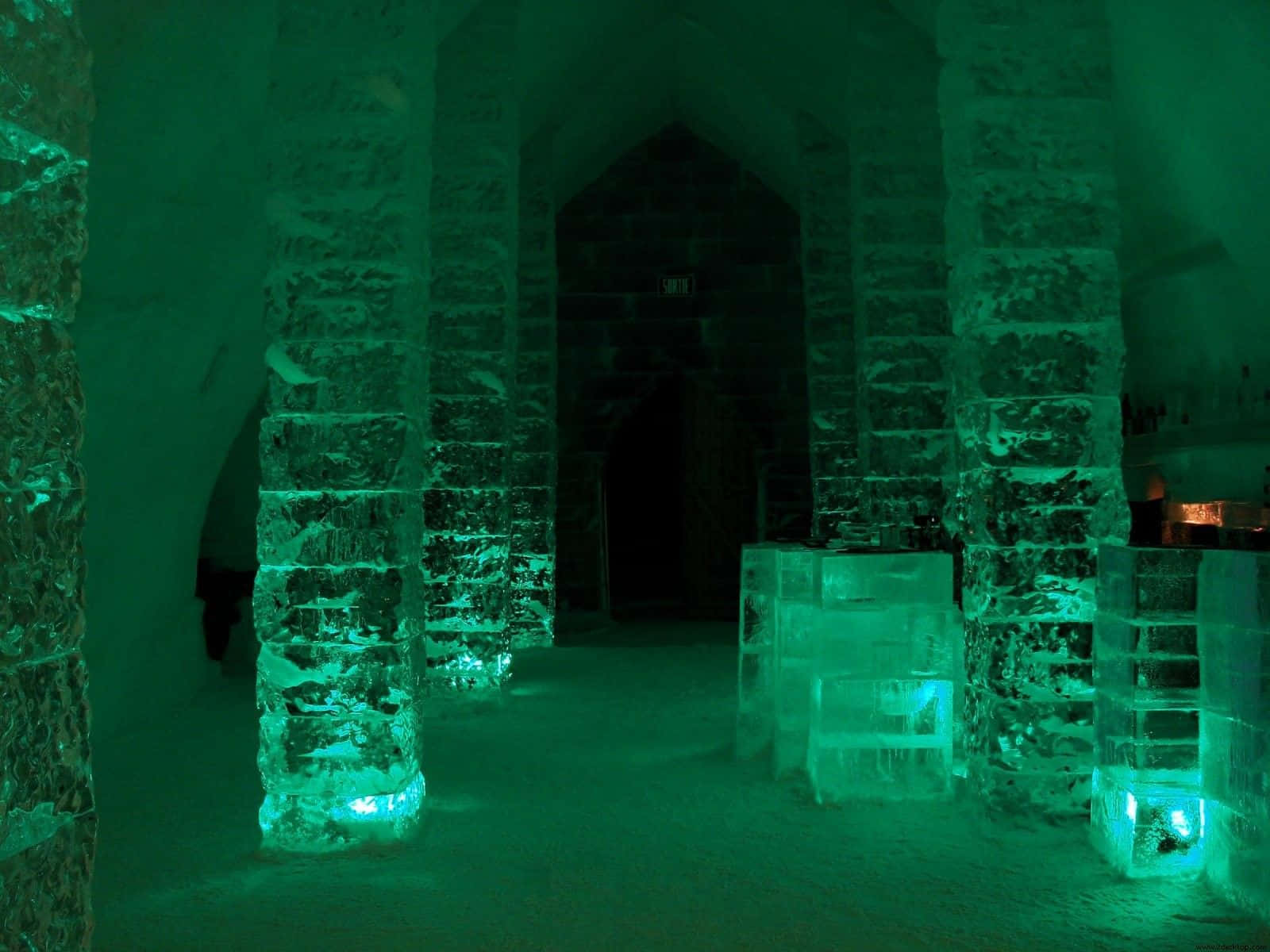 Ice Hotel 桌布 壁紙 — 冰雕的大教堂式內部，發光的綠色燈光照亮高聳的柱子和拱形門口。