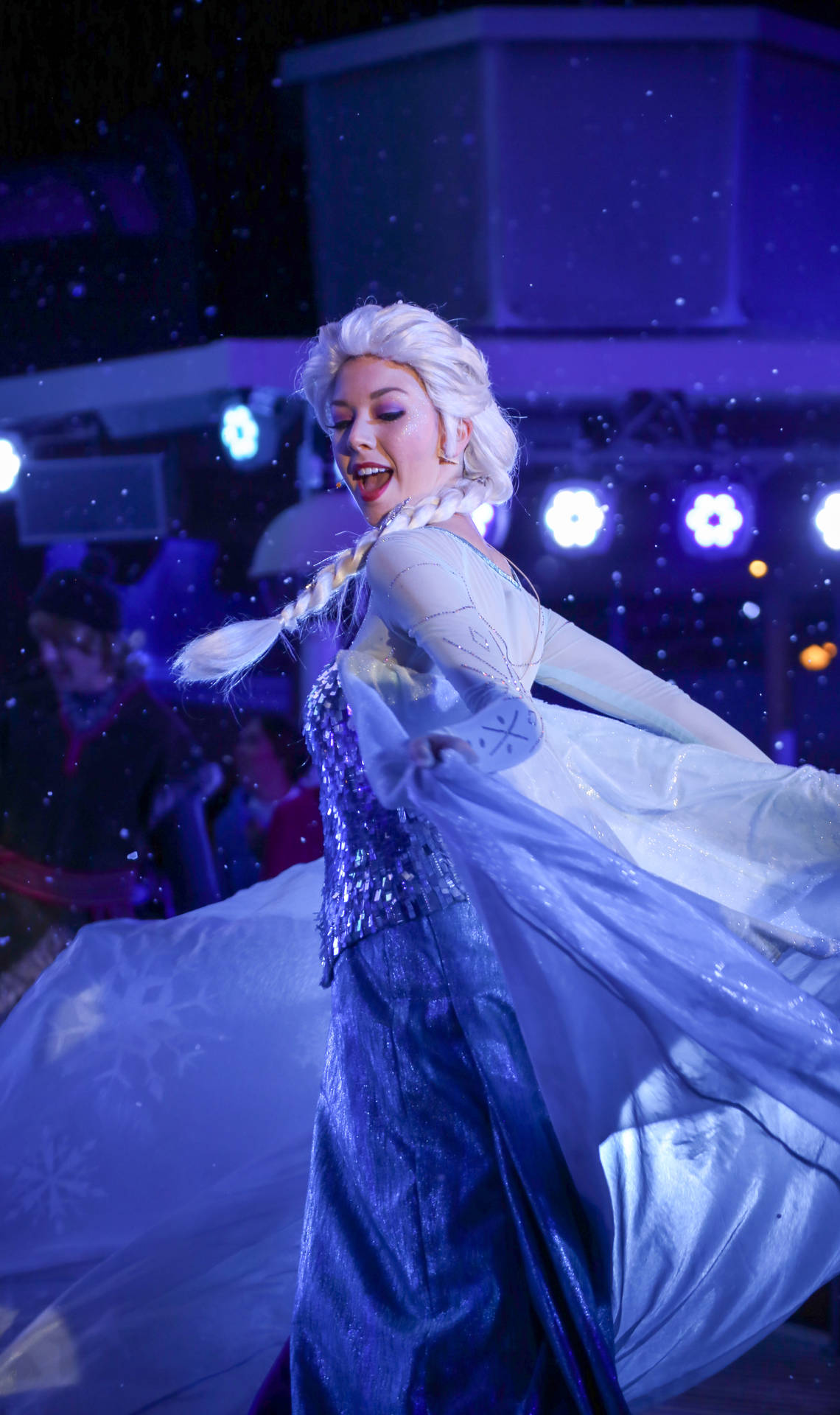 《冰雪奇緣》艾莎的角色扮演者在舞台燈光和雪效果下穿著藍色長裙跳舞。 — 迪士尼 壁紙