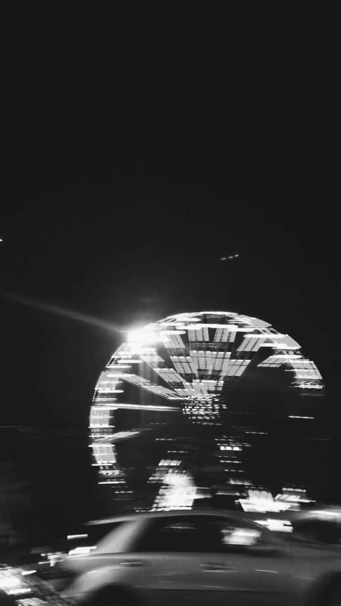 夜晚發光的摩天輪倒映在水中，一輛模糊的汽車駛過。