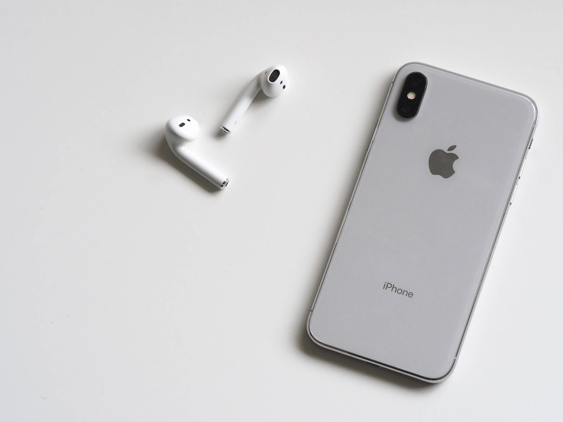 銀色 iPhone X 和白色 AirPods 在白色表面上。