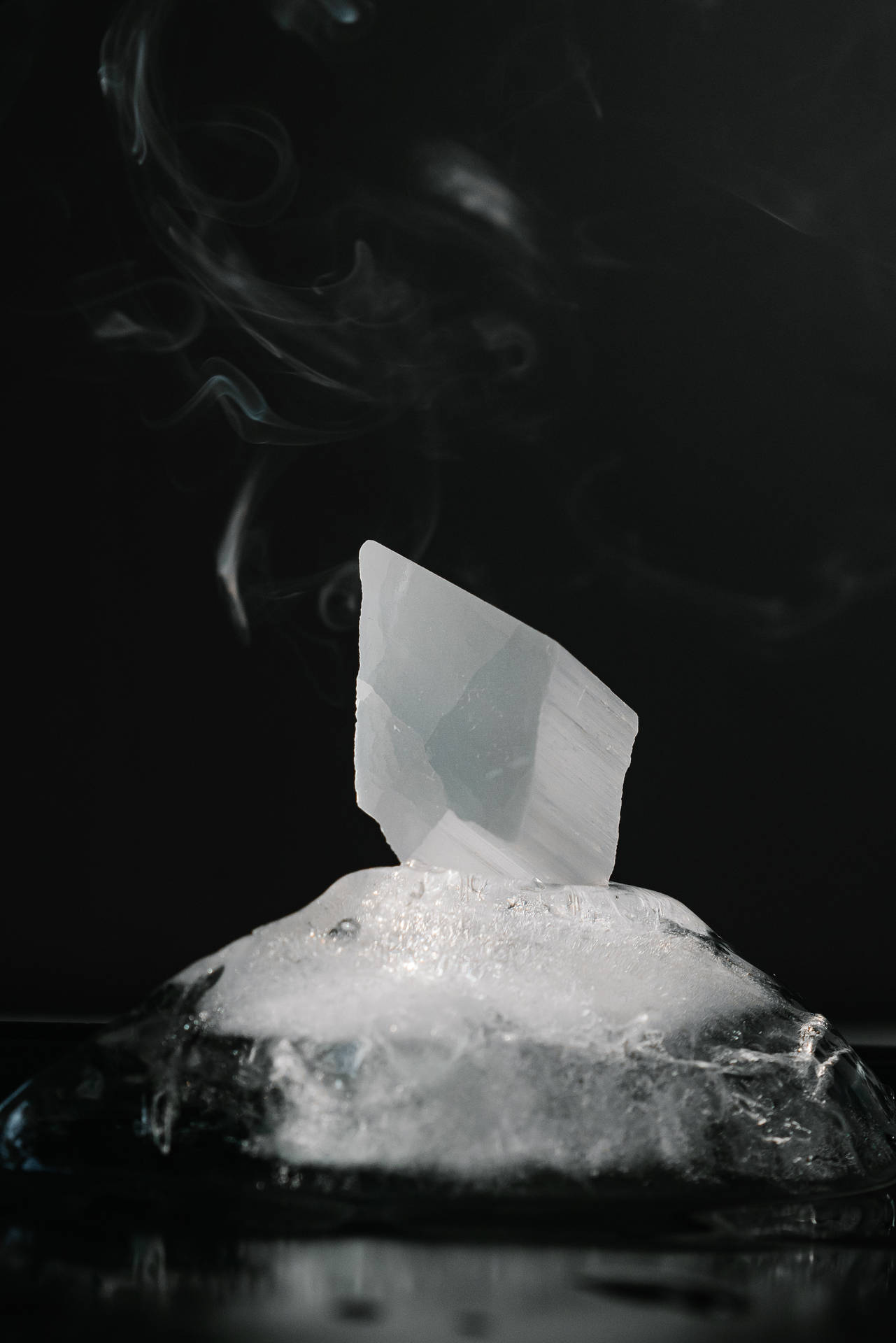 一顆從融冰中升起的晶體，煙霧在其上方旋轉，背景為深色表面。